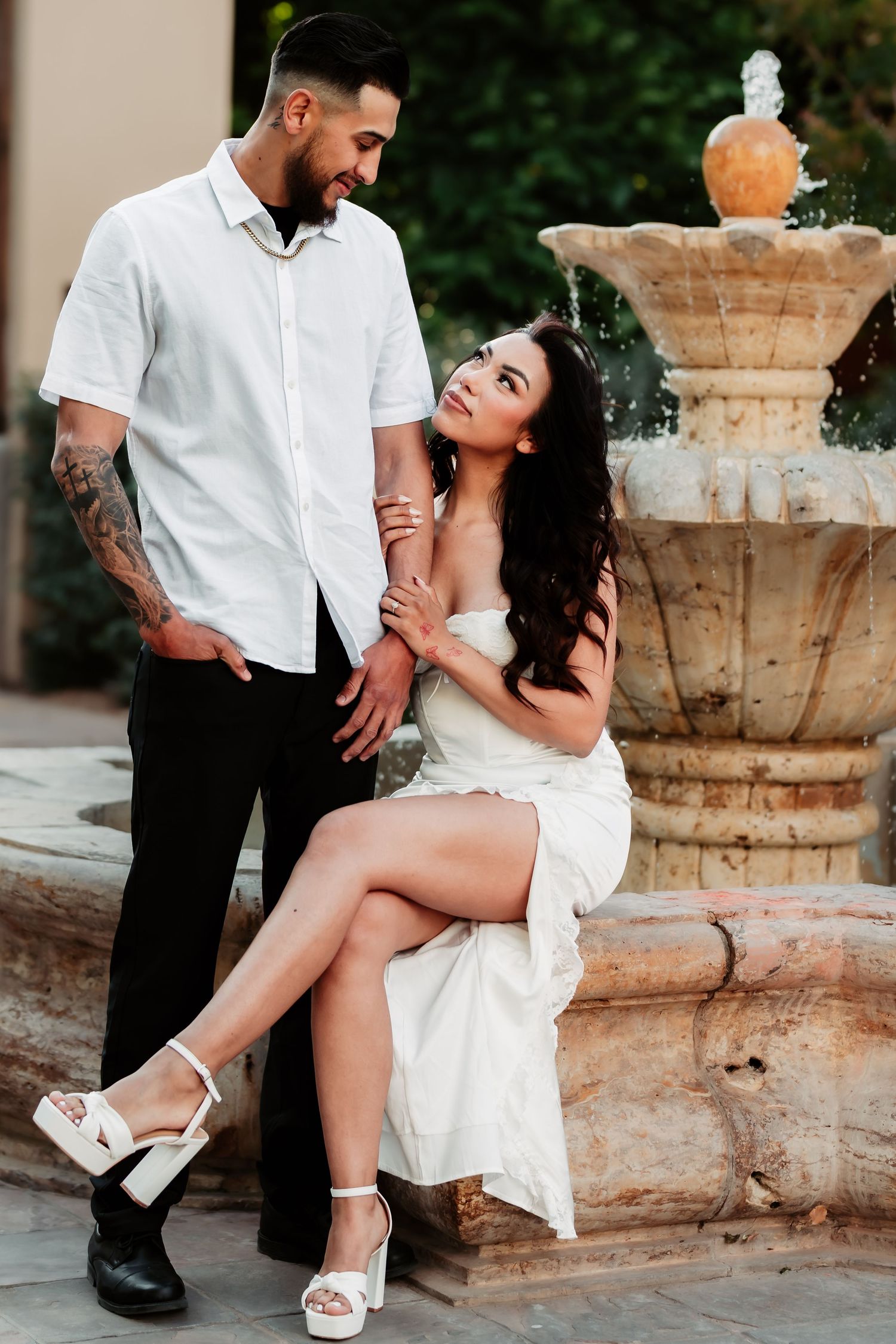 A couple shares a romantic moment while sitting by an ornate stone fountain during a photo session.