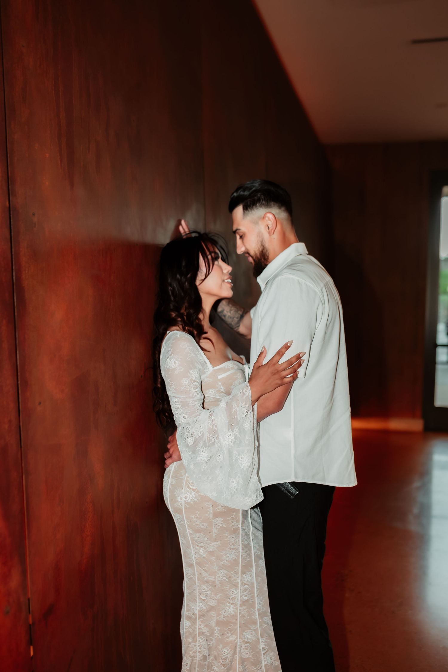 Intimate moment between couple against burgundy wall in moody lighting.