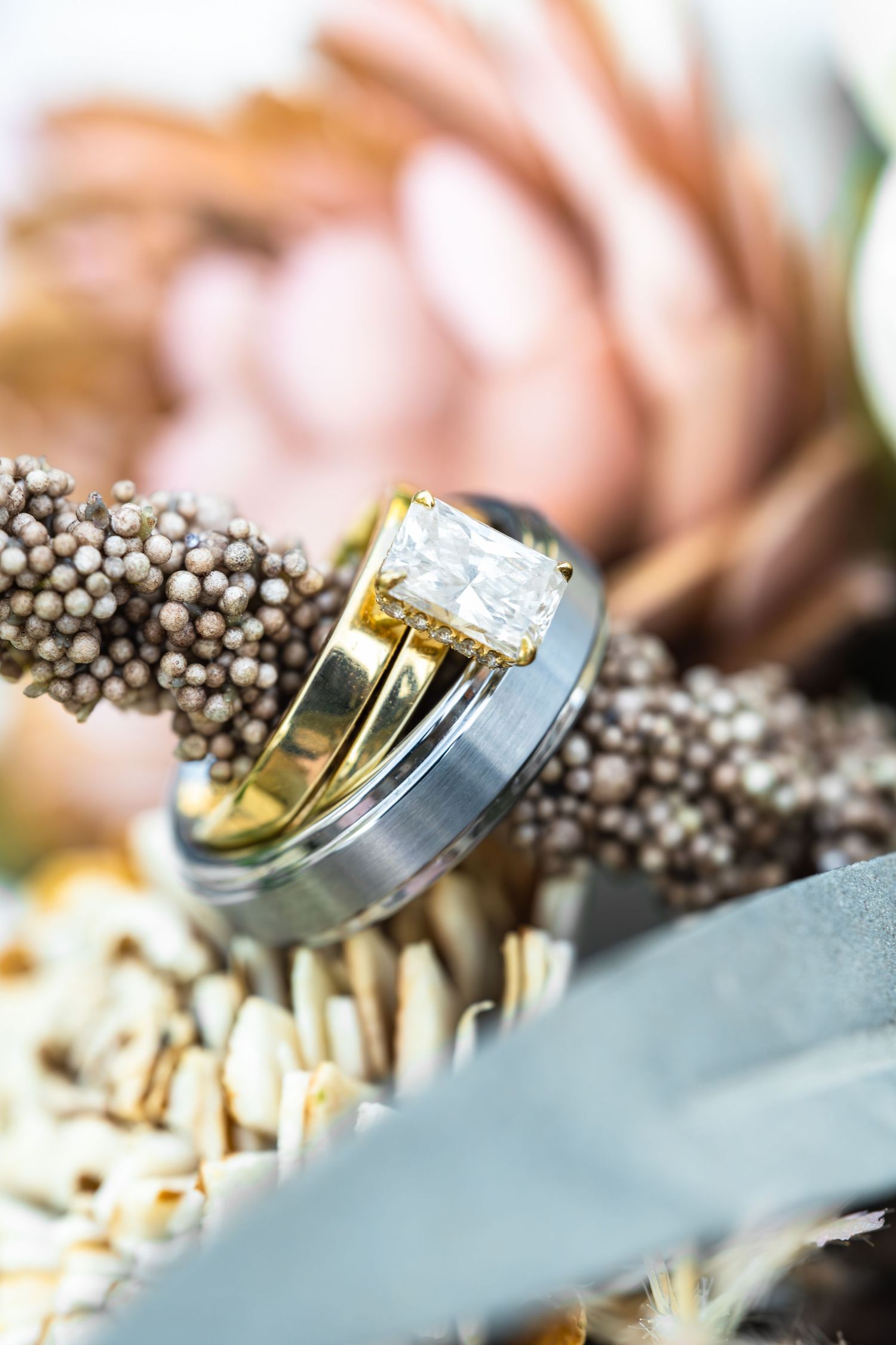Wedding rings displayed on dried flowers with diamond engagement ring in macro detail shot.