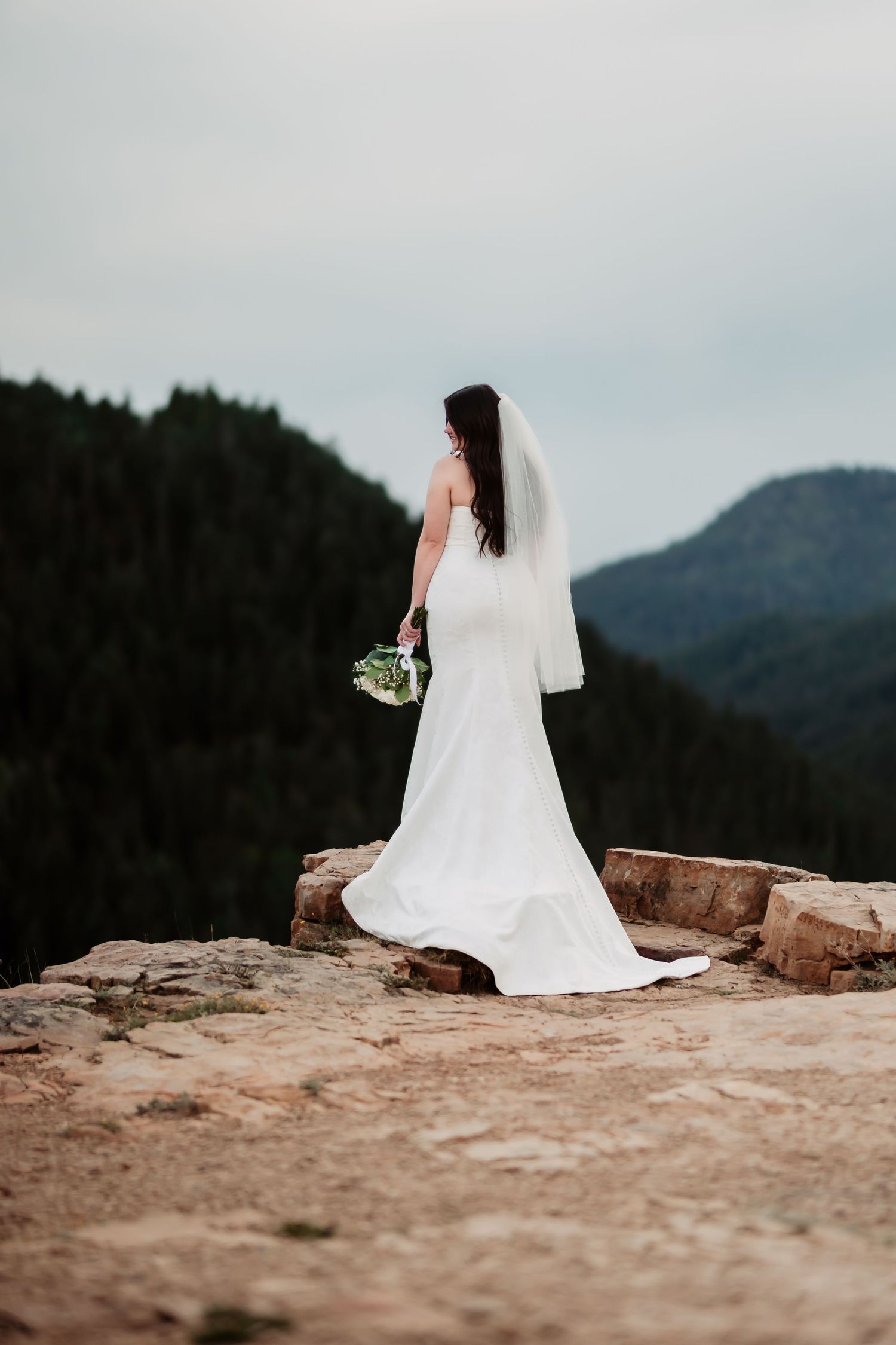 Elegant bridal portrait on rocky mountain ledge with dramatic mountain vista.