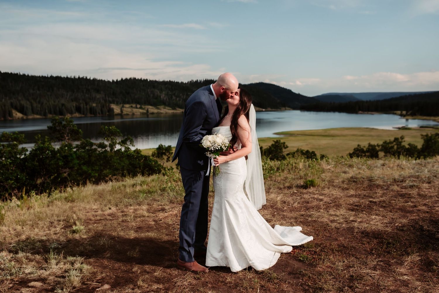 A romantic embrace during a mountain wedding with a lake vista in the background.