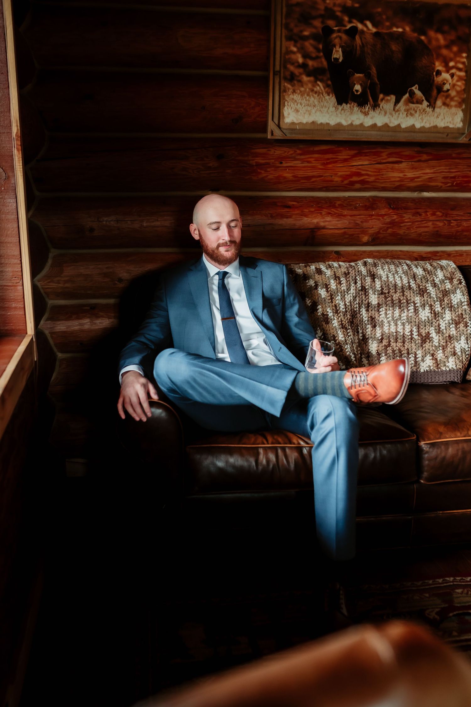 Side view of person in blue suit reclining on vintage patterned sofa against log cabin walls.