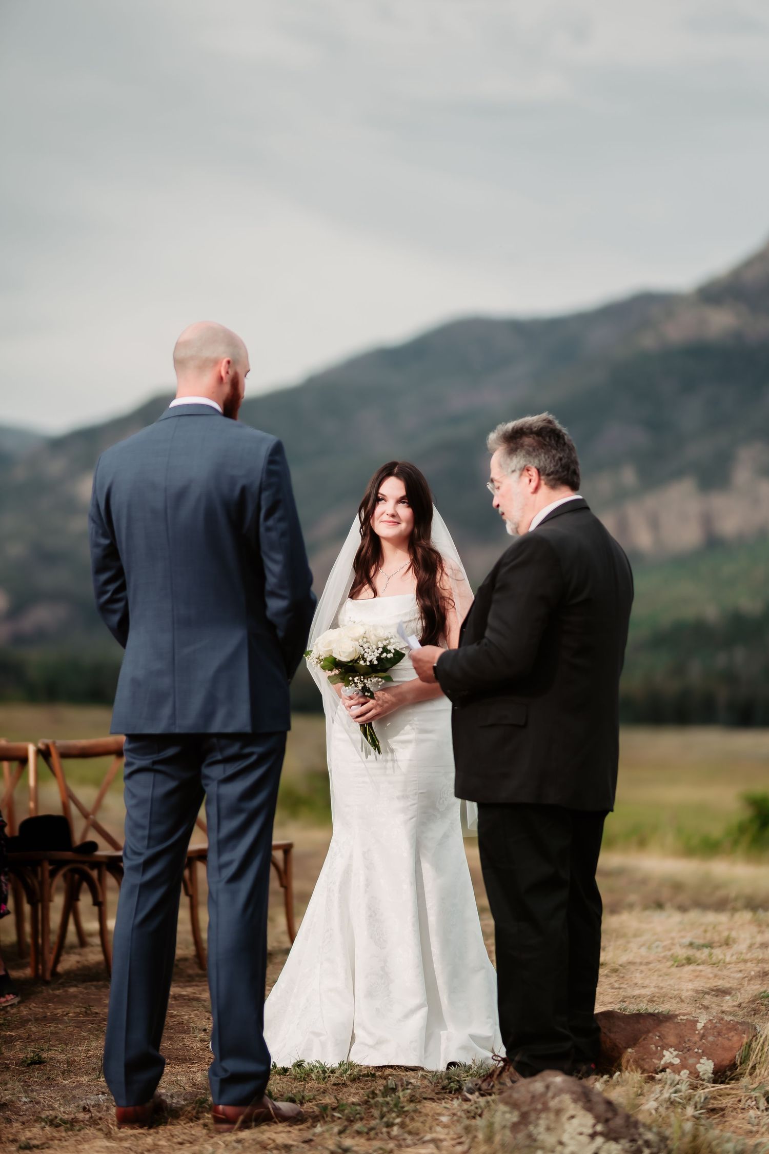 An outdoor wedding ceremony takes place against a backdrop of mountainous terrain and natural scenery.