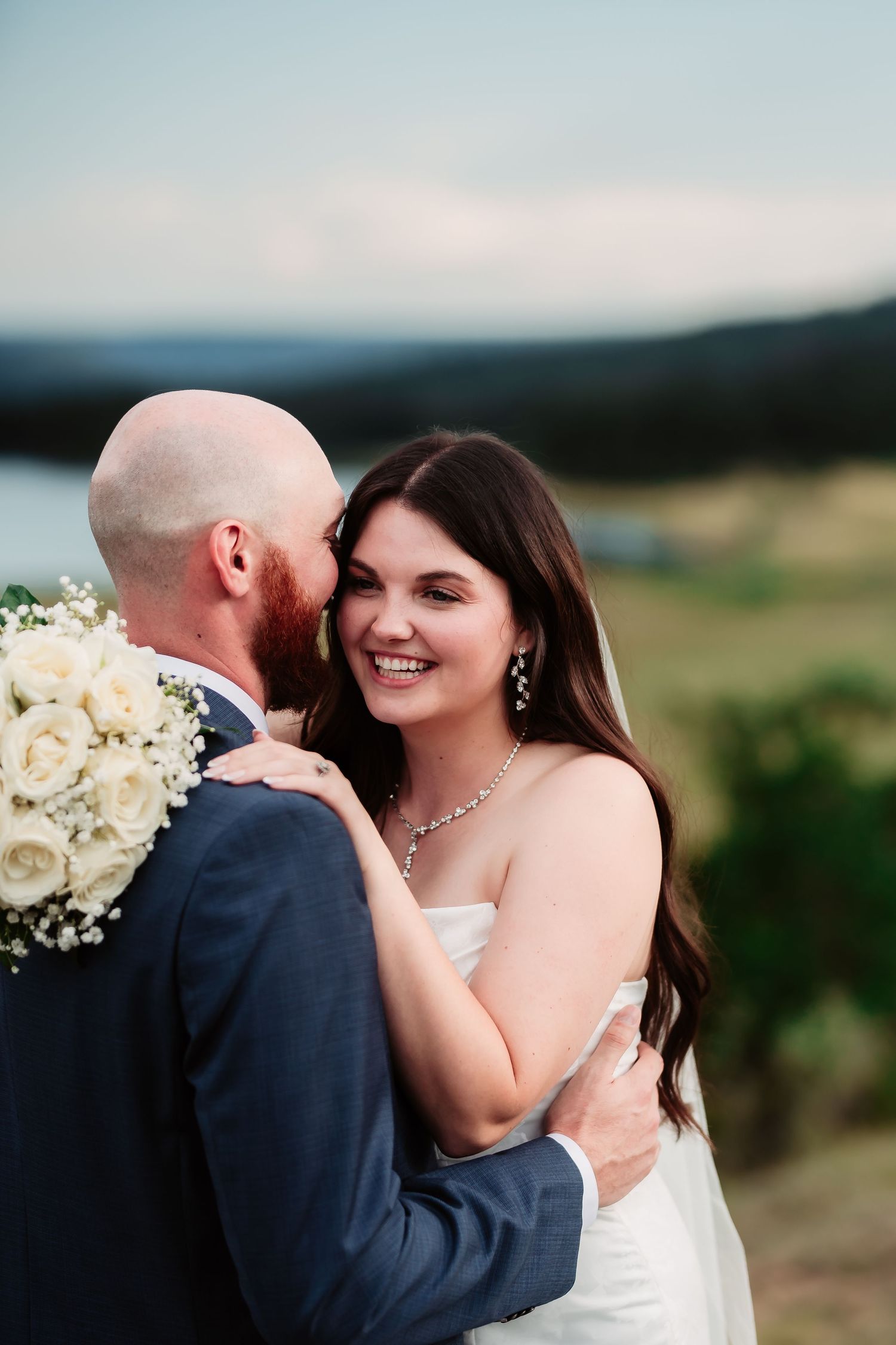 A tender moment between a couple on their wedding day with mountains and lake in the background.