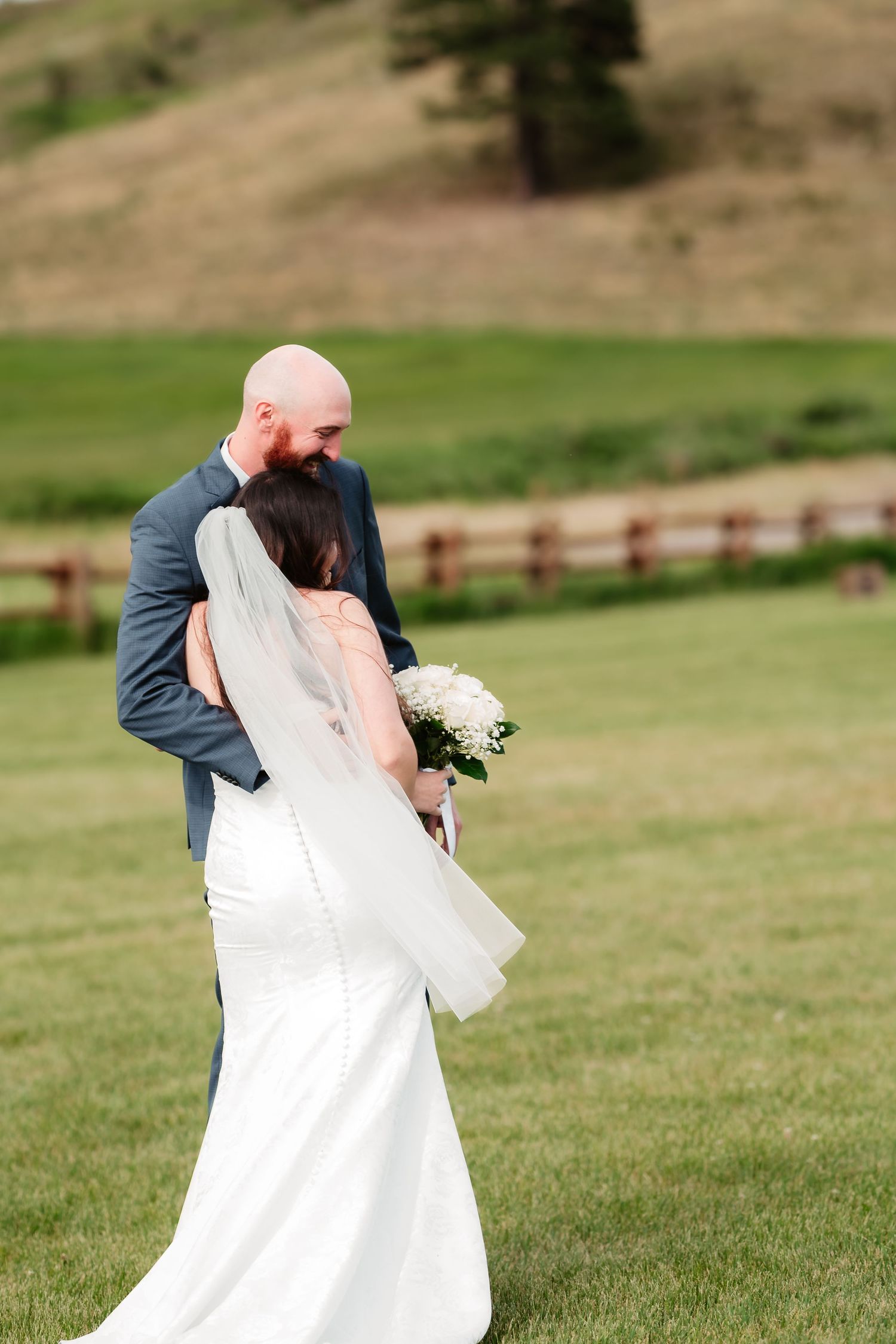 Bride and groom embrace on a grassy hillside with rolling landscape in the background.