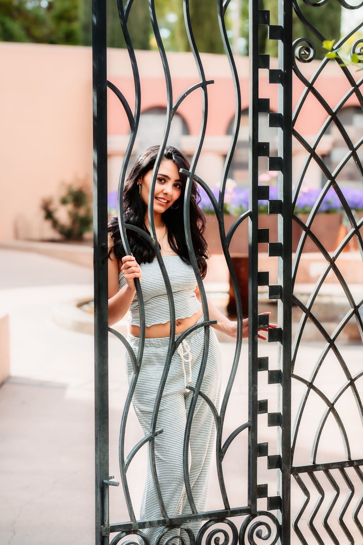 A playful pose at an ornate metal gate wearing a casual striped two-piece outfit.