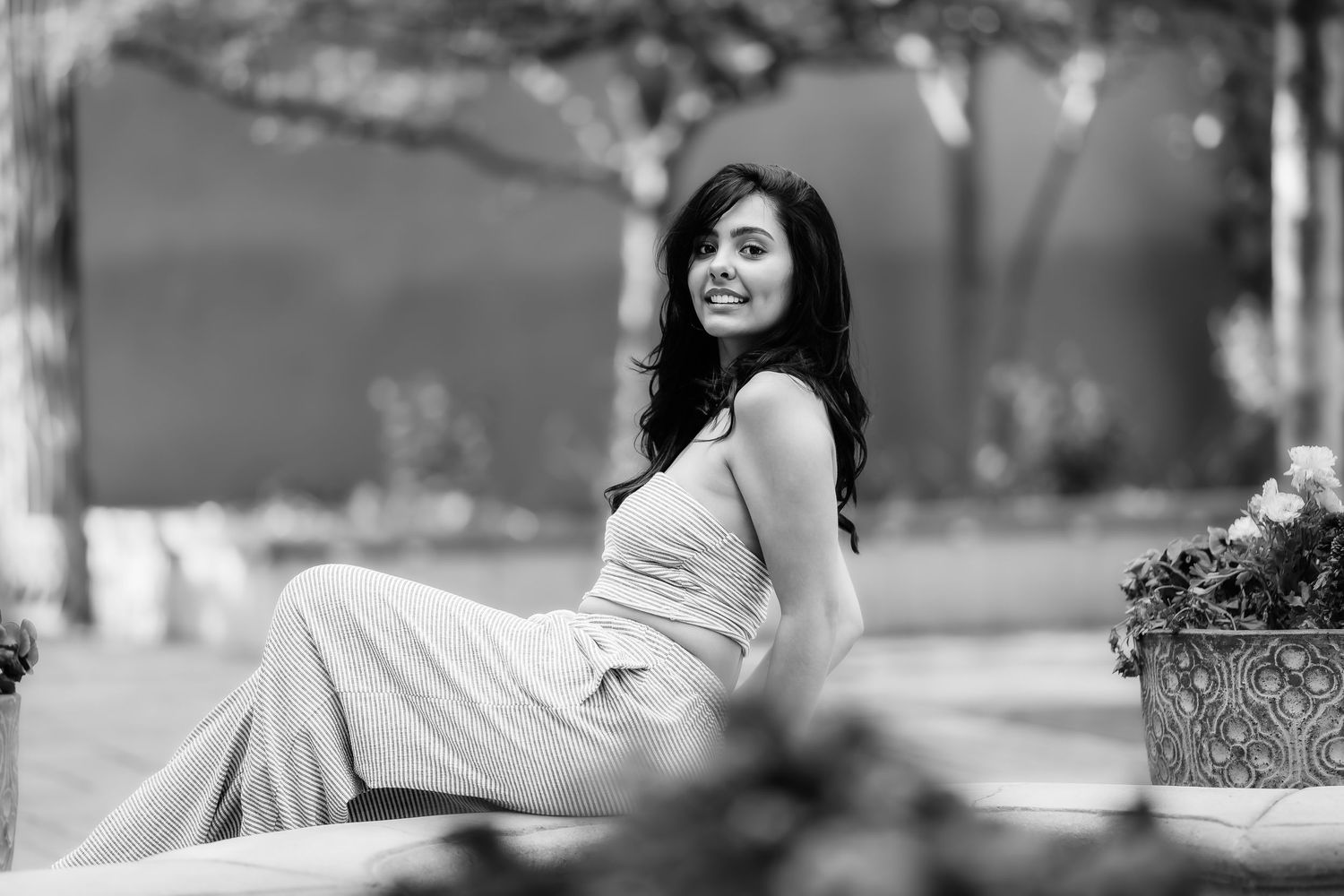 Black and white portrait of person in casual dress relaxing outdoors near planters.