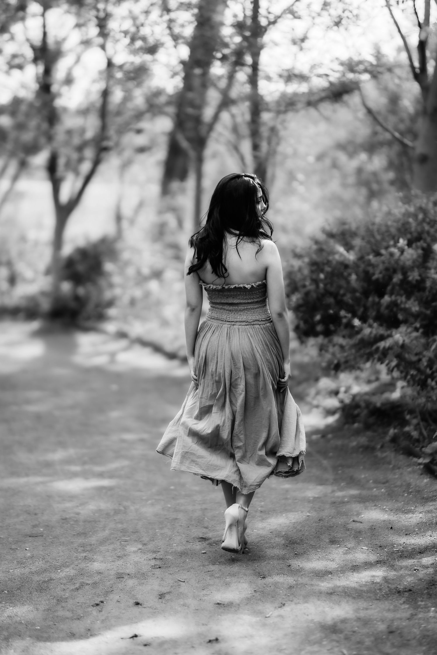 Black and white image of person in flowing dress walking along garden path.