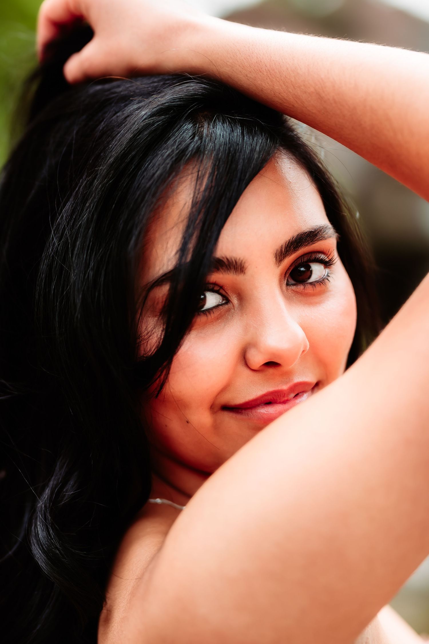 A close-up portrait shows dark flowing hair and a warm smile in natural lighting.