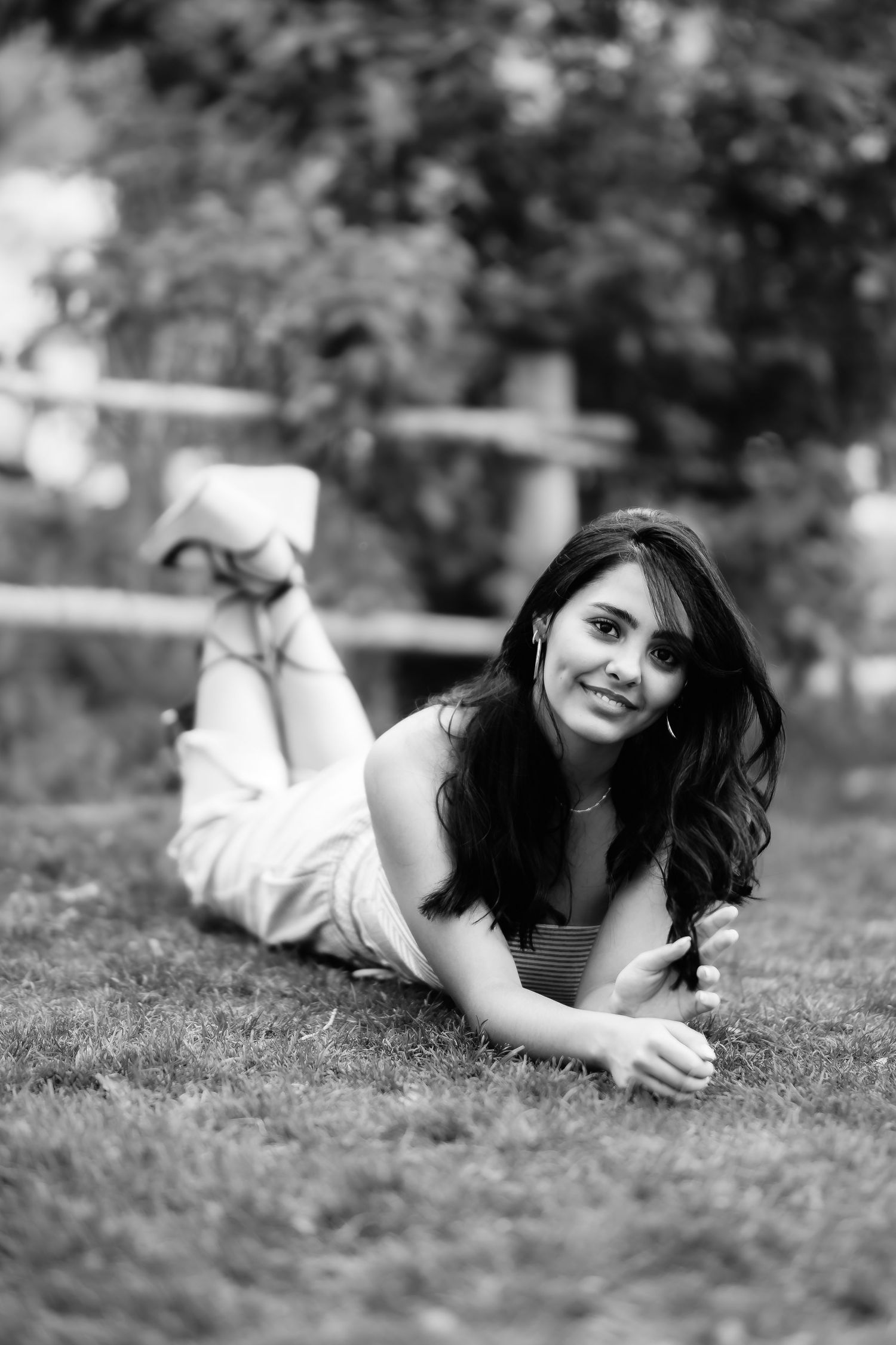 Black and white portrait of someone lying on grass outdoors in casual attire with a relaxed pose.