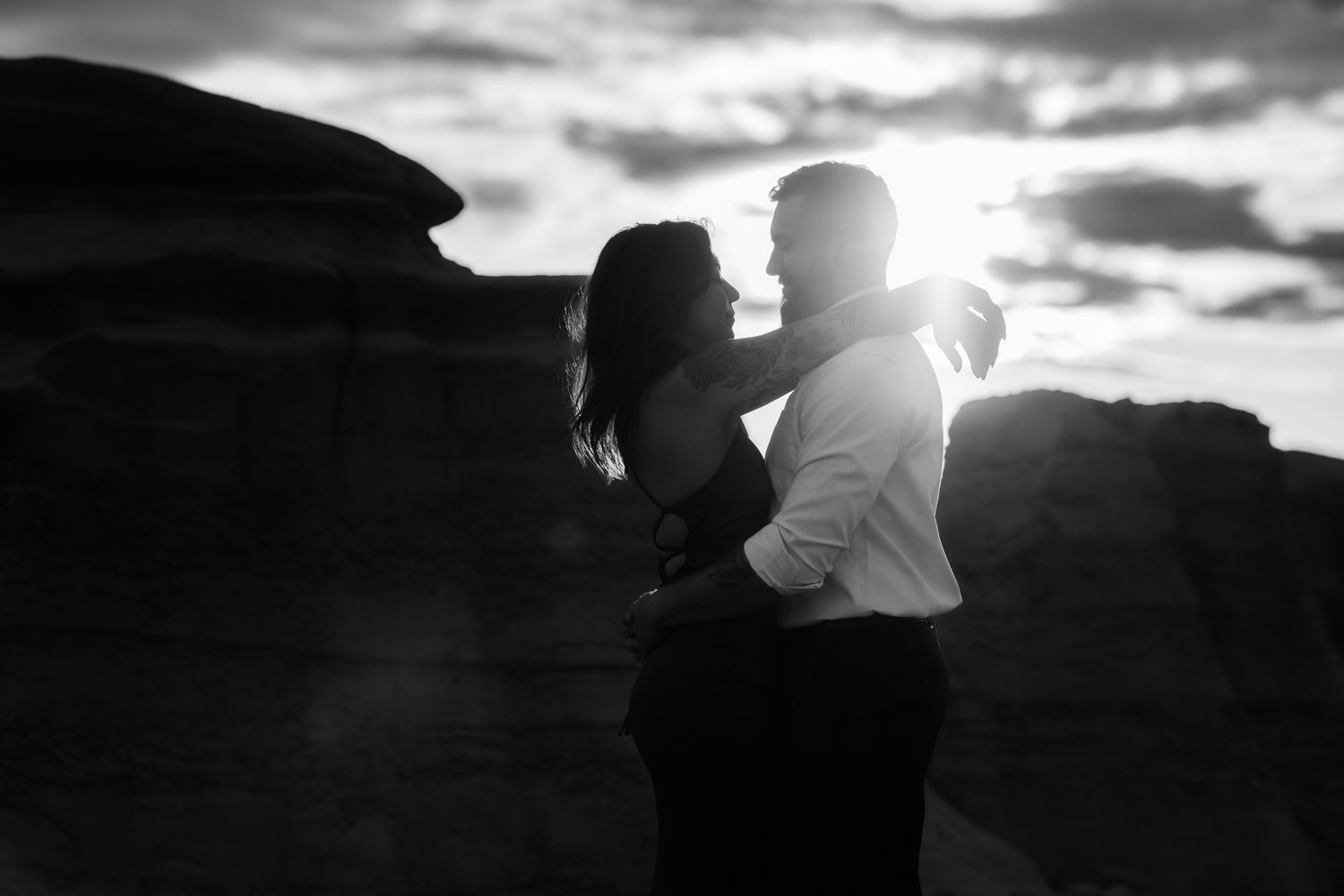 A silhouetted couple embraces against a dramatic sunset sky over desert rock formations.