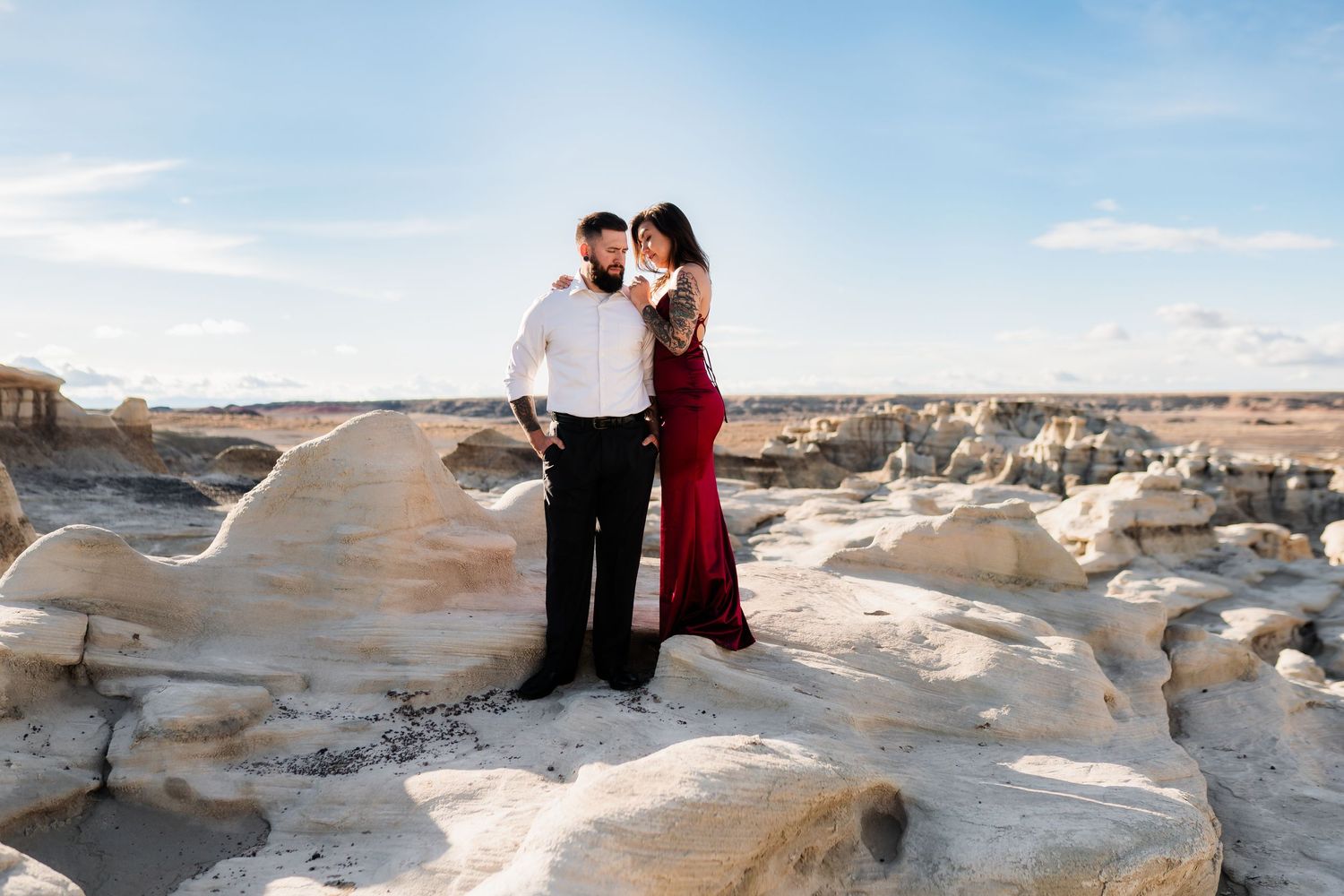 Romantic couple standing on white rock formations in desert landscape under blue sky.