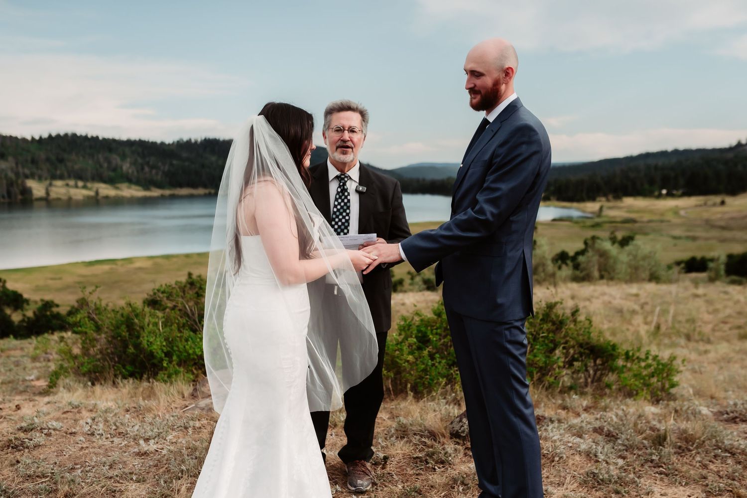 Outdoor wedding ceremony in a scenic mountain meadow with wooden cross-back chairs.