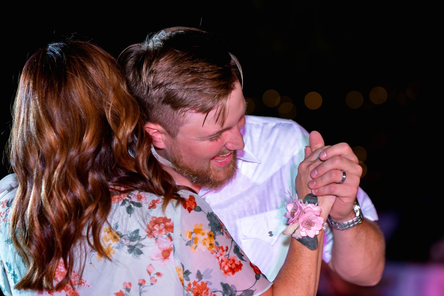 Couple dancing intimately under evening lights at wedding reception.