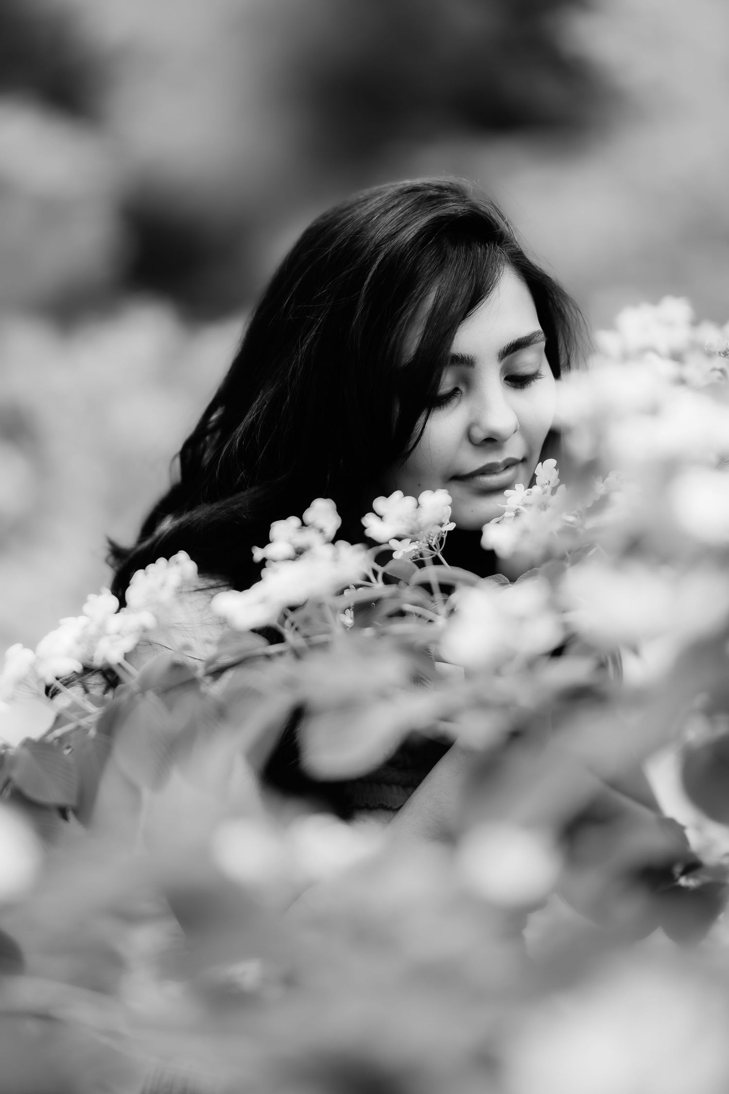 Artistic black and white photo of woman with dark hair among blooming white flowers.