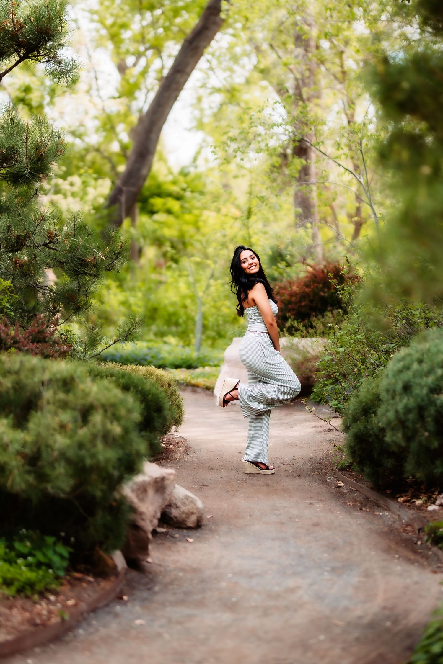 Playful pose on a garden path surrounded by green foliage and trees.