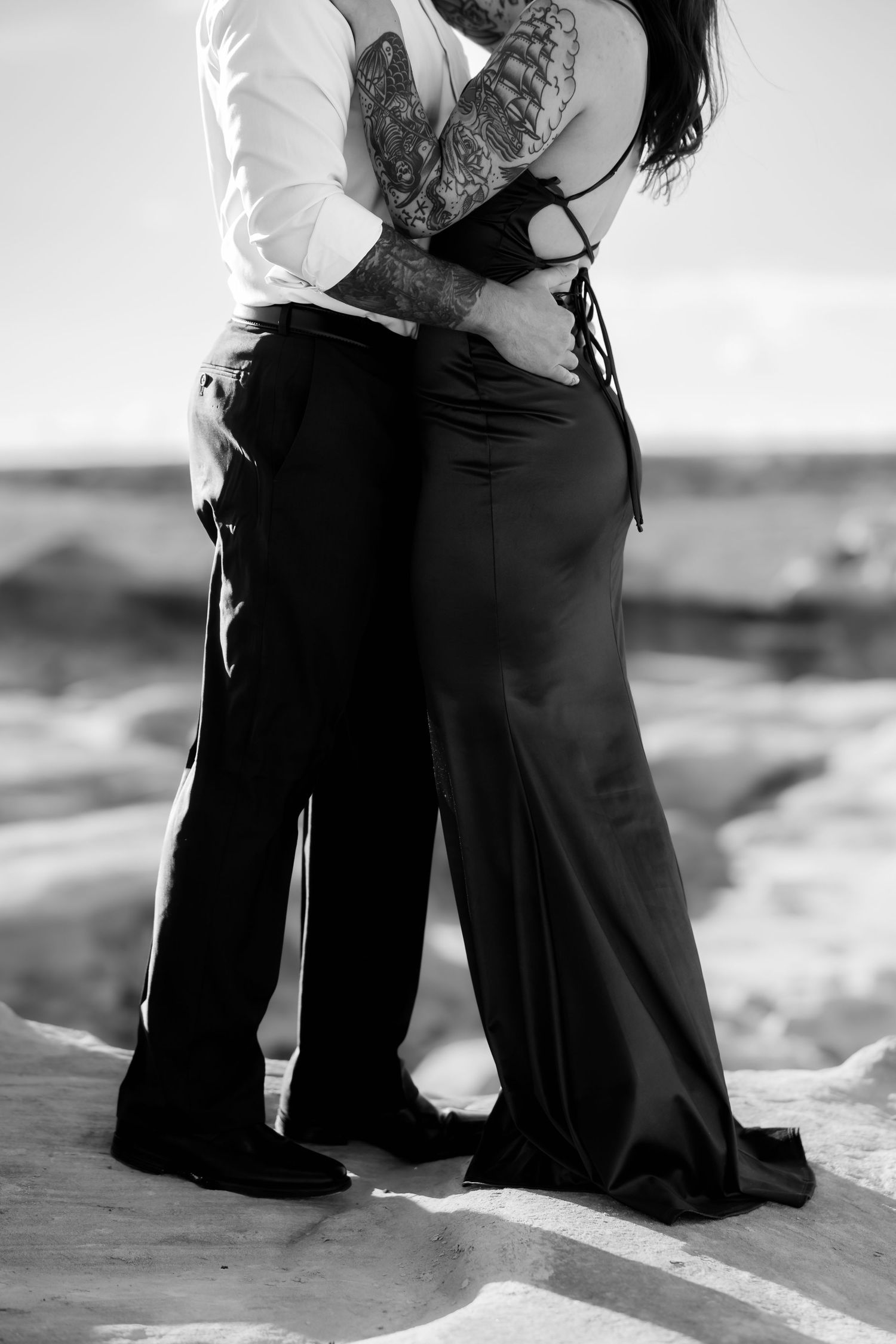 Black and white photo of a couple's embrace showing intricate tattoo details and formal attire.