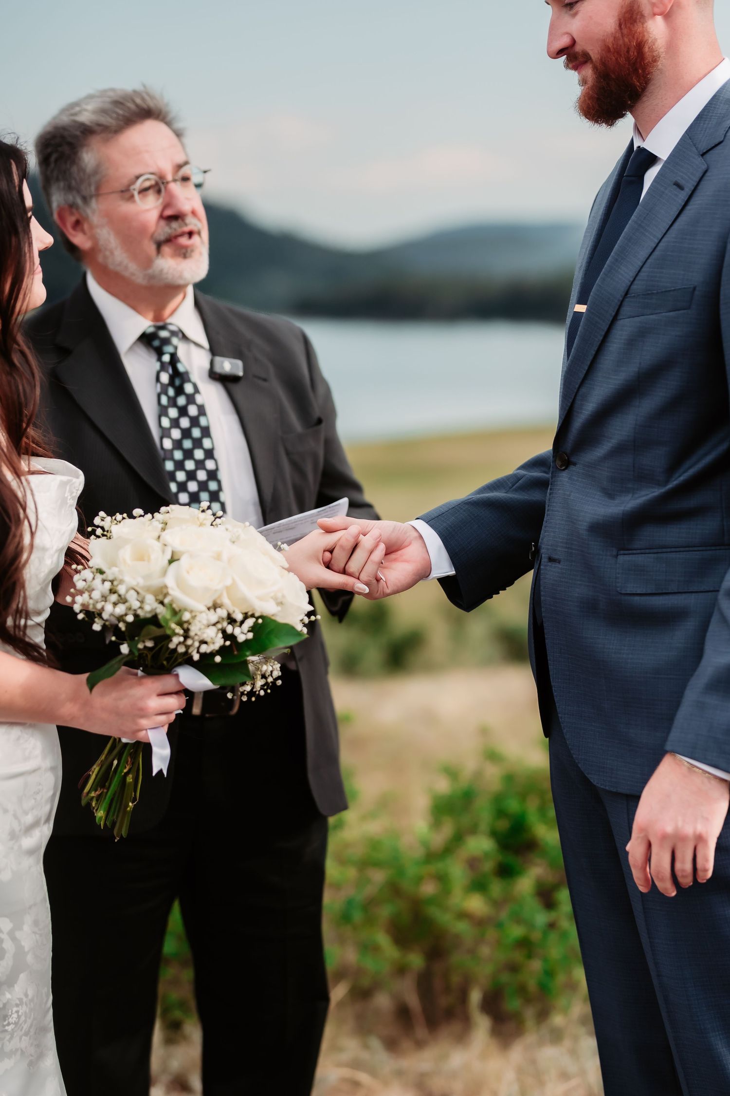 Wedding ceremony participants exchanging rings outdoors with scenic mountains in the background.