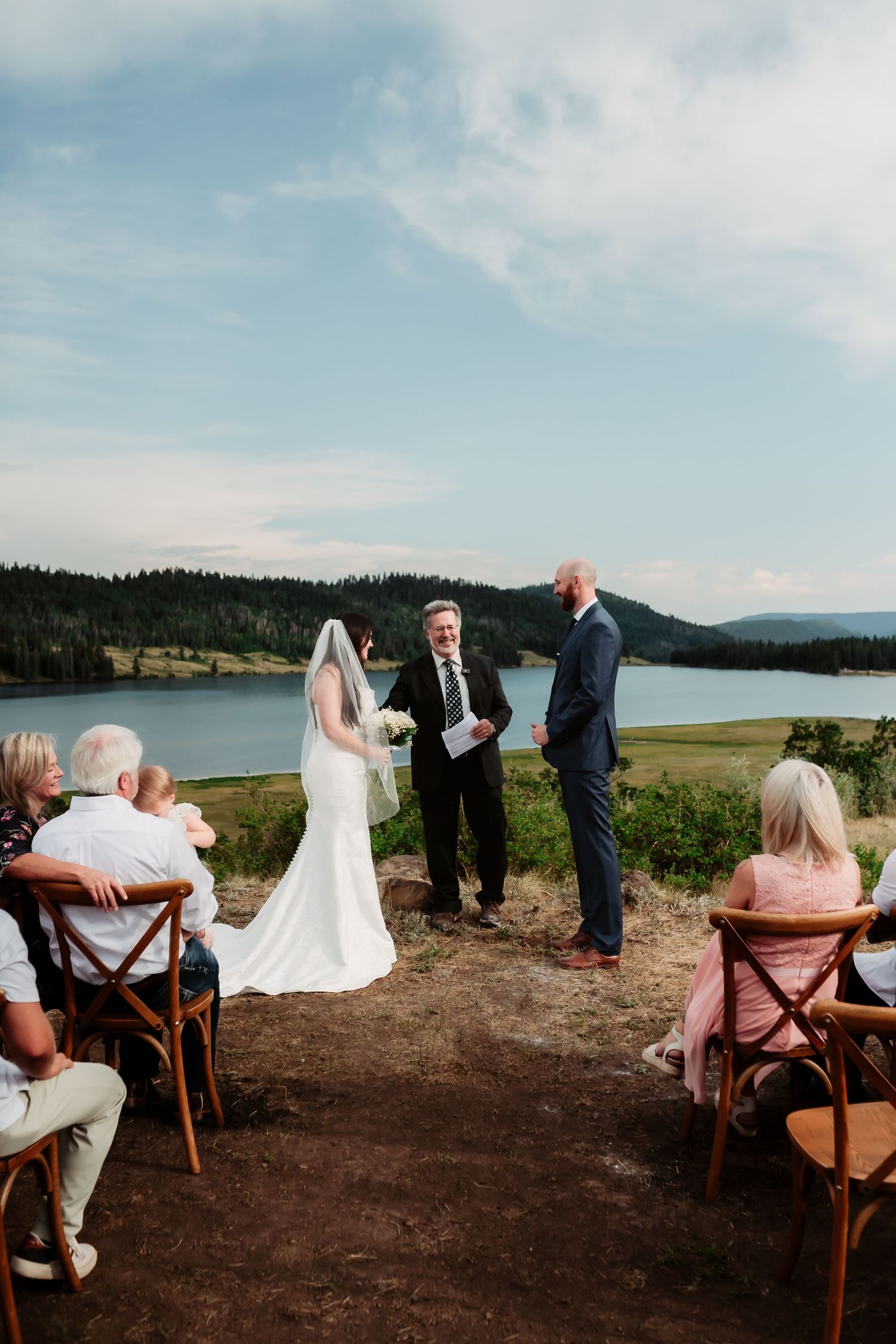 An intimate outdoor wedding ceremony overlooking a lake with wooden chairs and natural scenery.