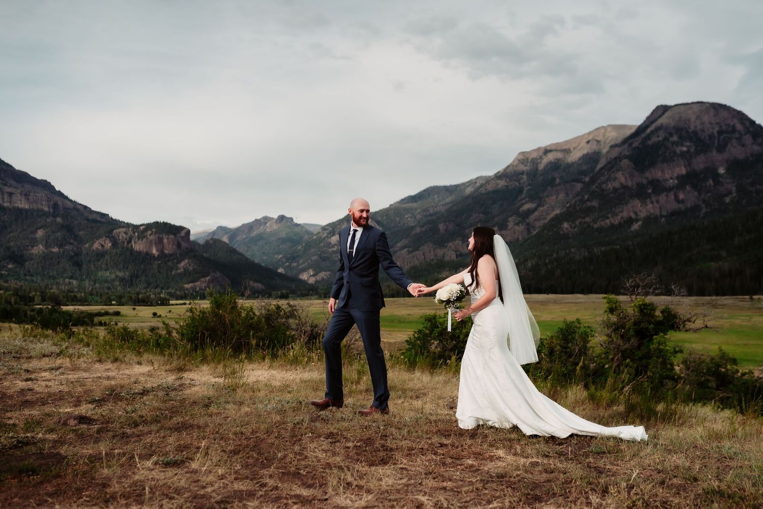 A couple shares a playful moment dancing together on a mountainside during their wedding.