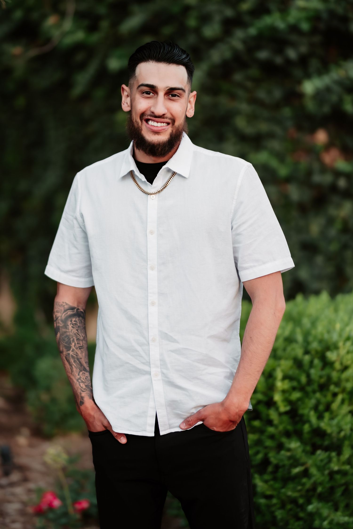 Portrait of a man in white button-down shirt smiling at camera with greenery background.