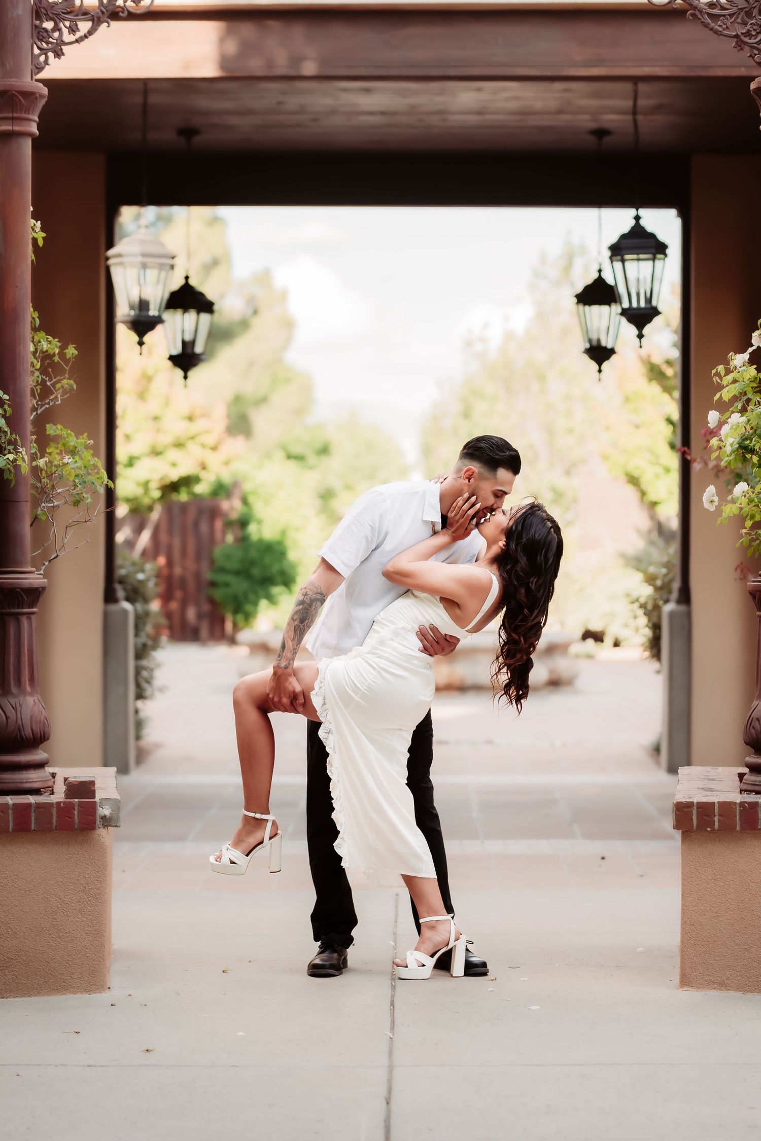 A romantic dip pose sequence under a covered walkway with hanging lanterns and brown pillars.