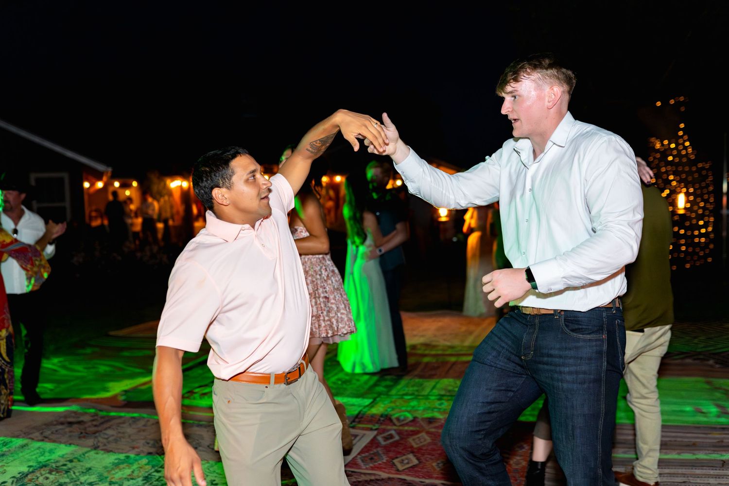 Wedding guests dancing and celebrating on an illuminated outdoor dance floor at night.