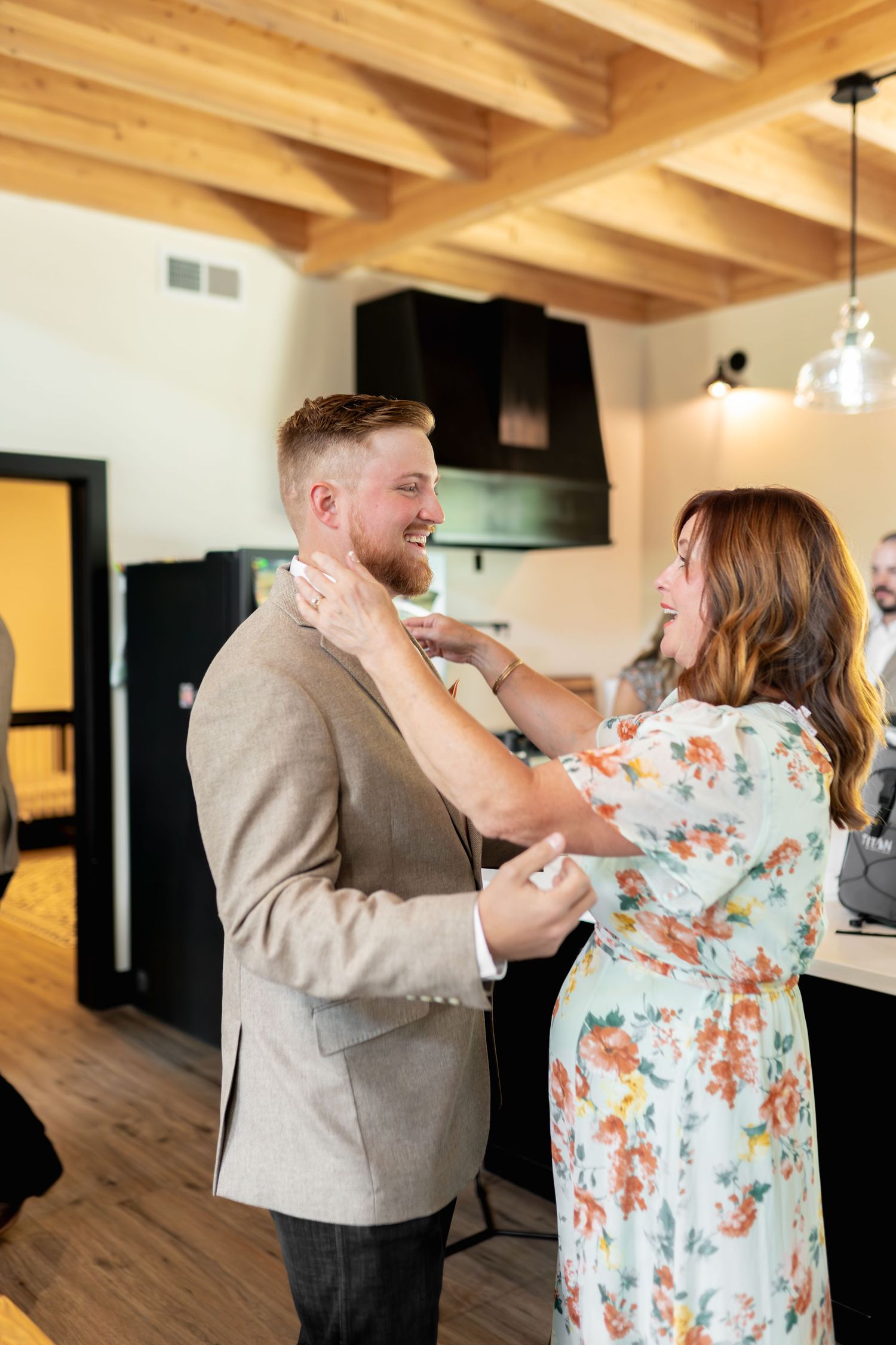 Couple sharing tender moment in rustic kitchen with wood beam ceiling and pendant lighting.