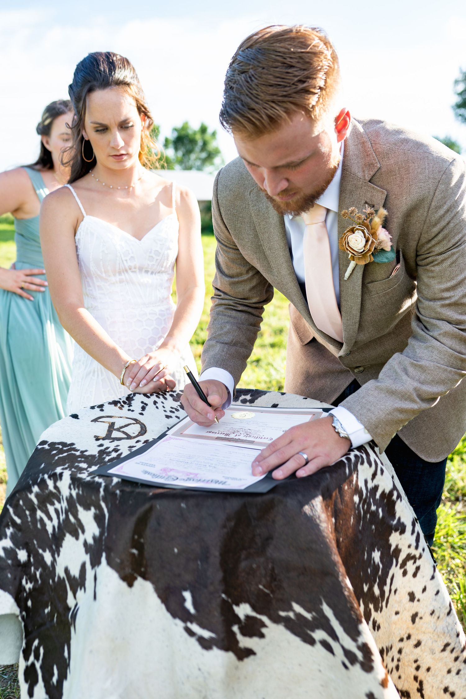 A couple signs their wedding certificate using a unique spotted cowhide table during an outdoor ceremony.