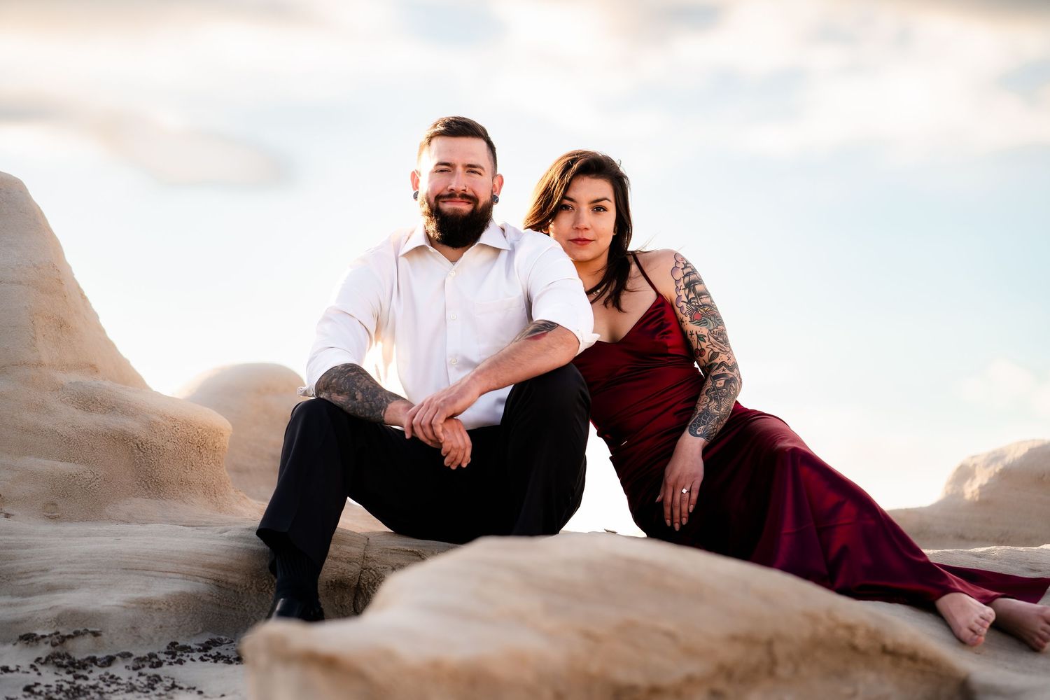 A couple in formal attire poses together on desert rocks during golden hour.
