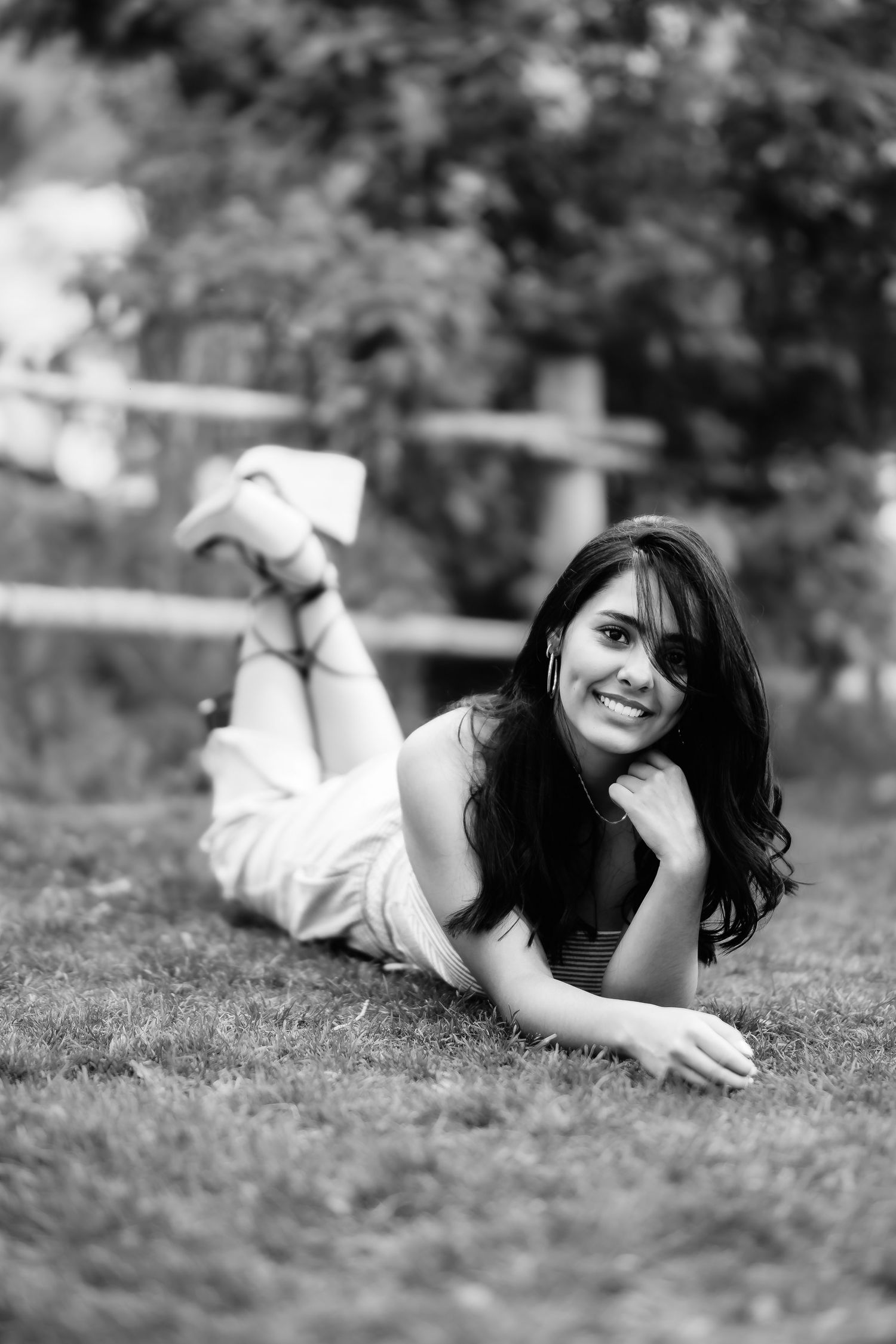 Black and white portrait of woman lying on grass and smiling at camera.