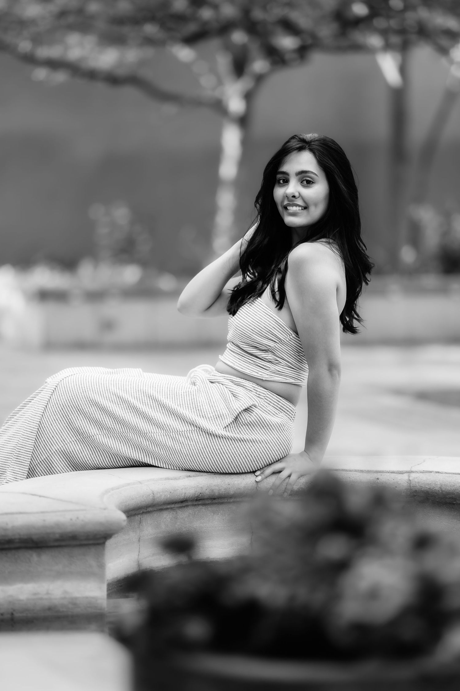 A black and white outdoor portrait features someone in a light dress seated on stone steps.