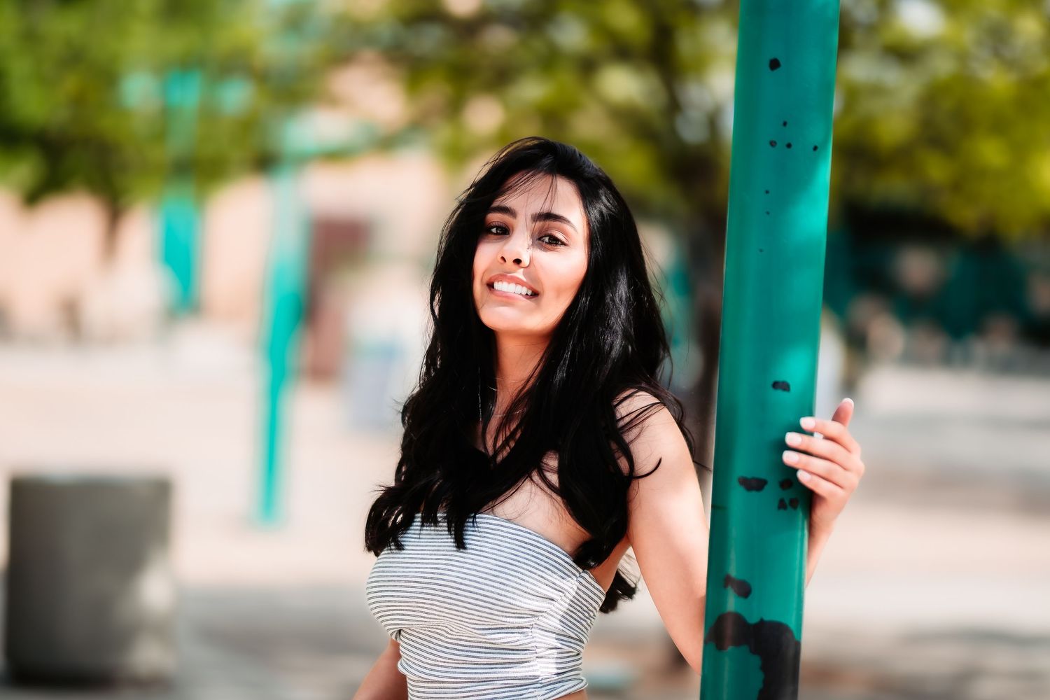 Woman in white dress poses playfully next to teal pole outdoors.