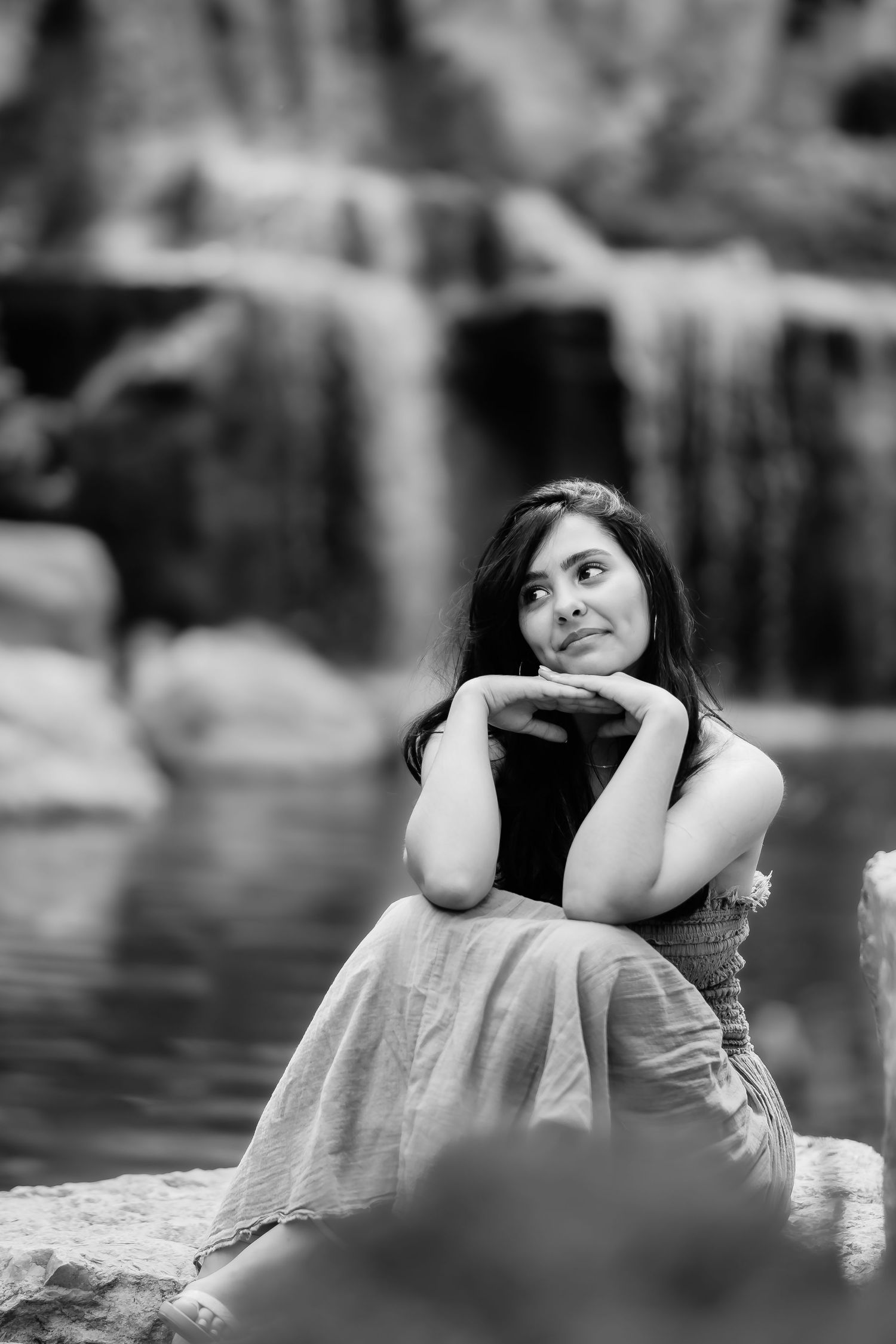 A black and white portrait of someone sitting thoughtfully near a waterfall.