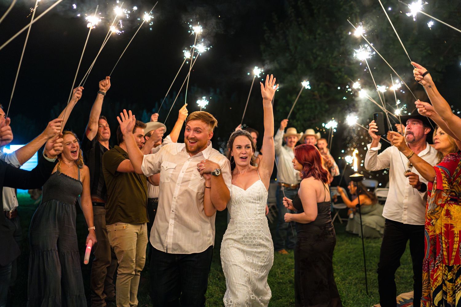 Wedding guests celebrate with sparklers raised high during an outdoor evening reception.