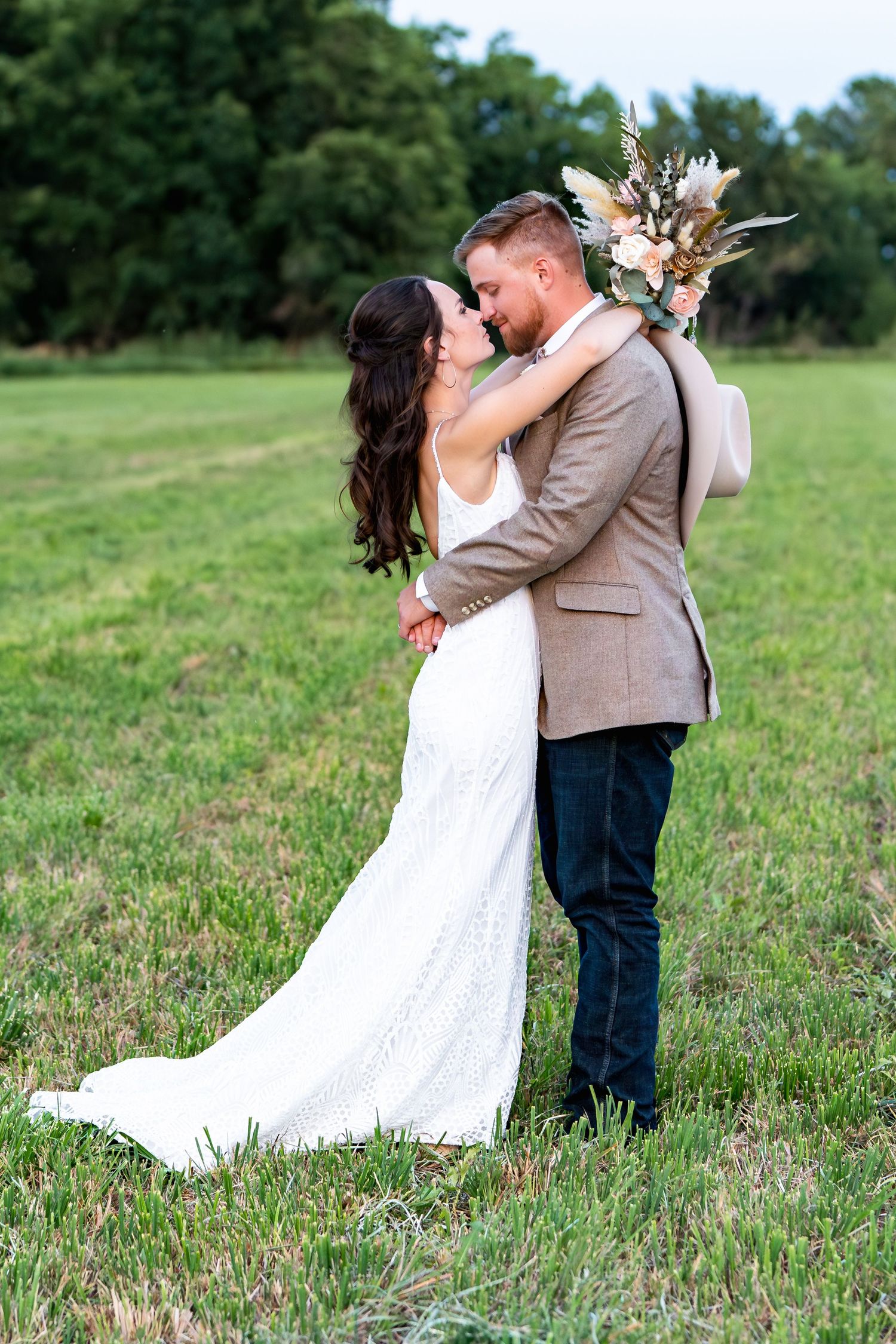 Newlyweds share an intimate moment in a grassy field with dried floral bouquet.