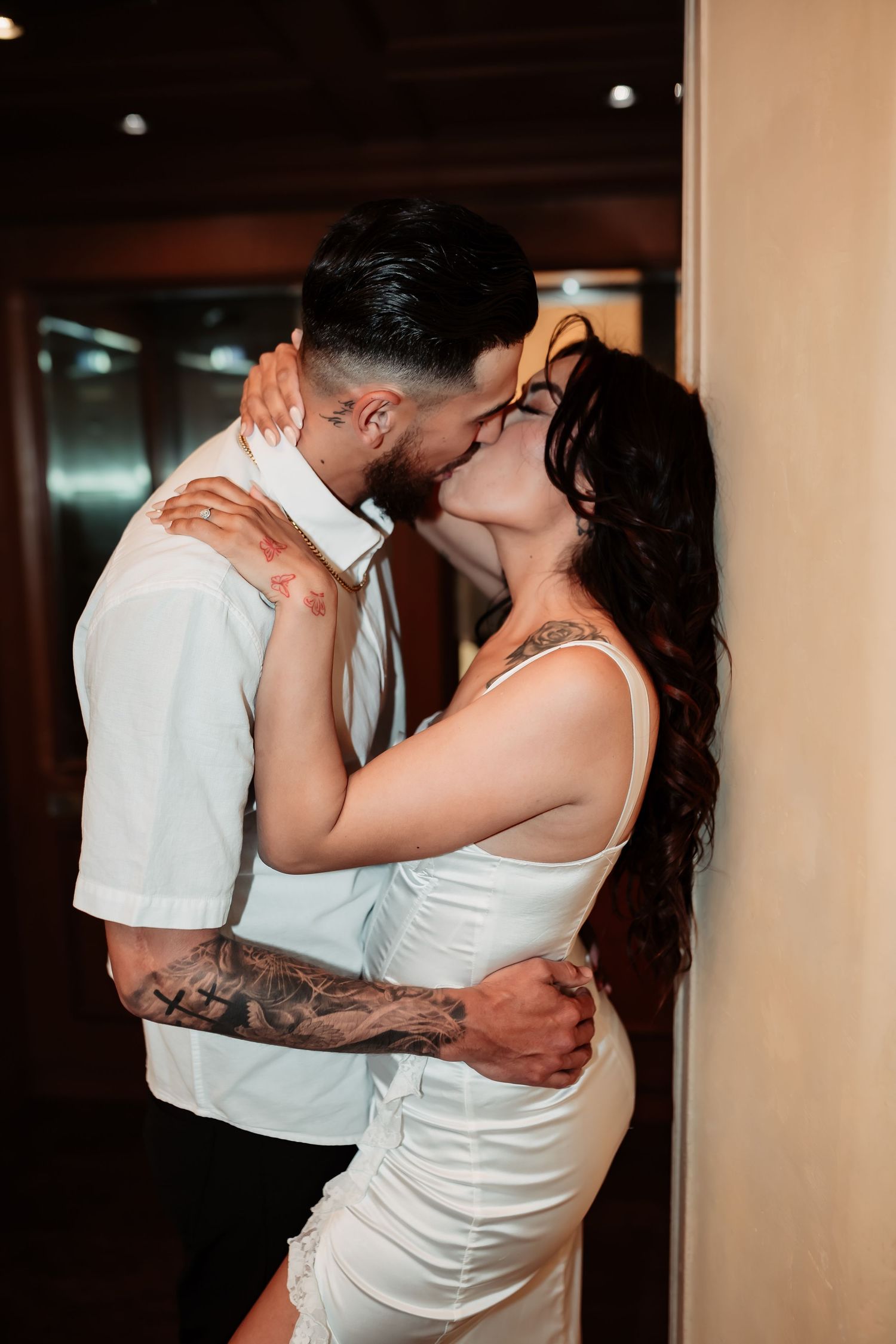 A couple in matching white outfits share a passionate kiss against a wall.