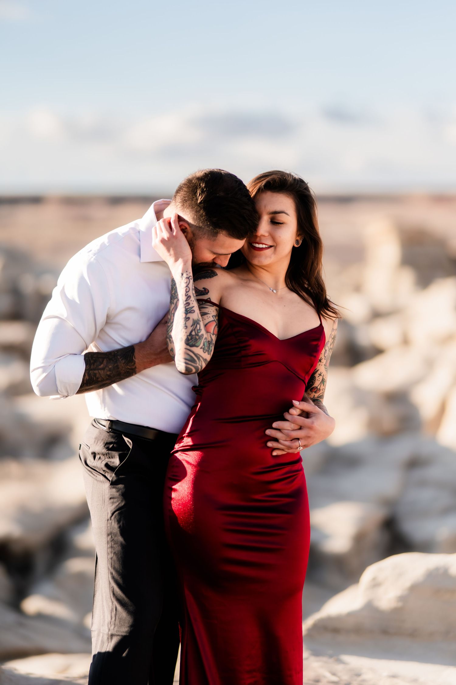 Romantic couple embraces on desert rocks at sunset with soft lighting.