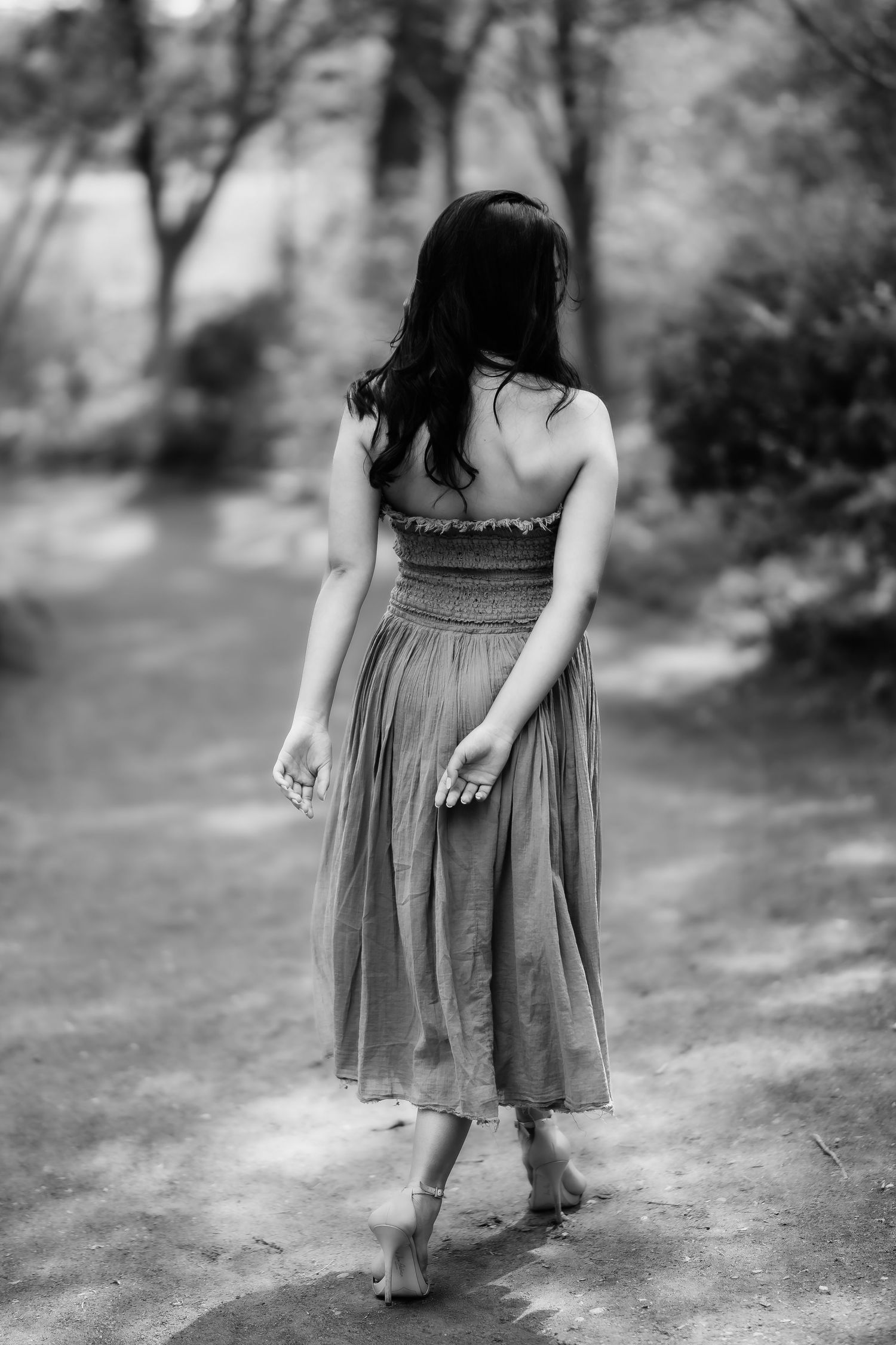 Black and white image of woman in dress walking barefoot on garden path.
