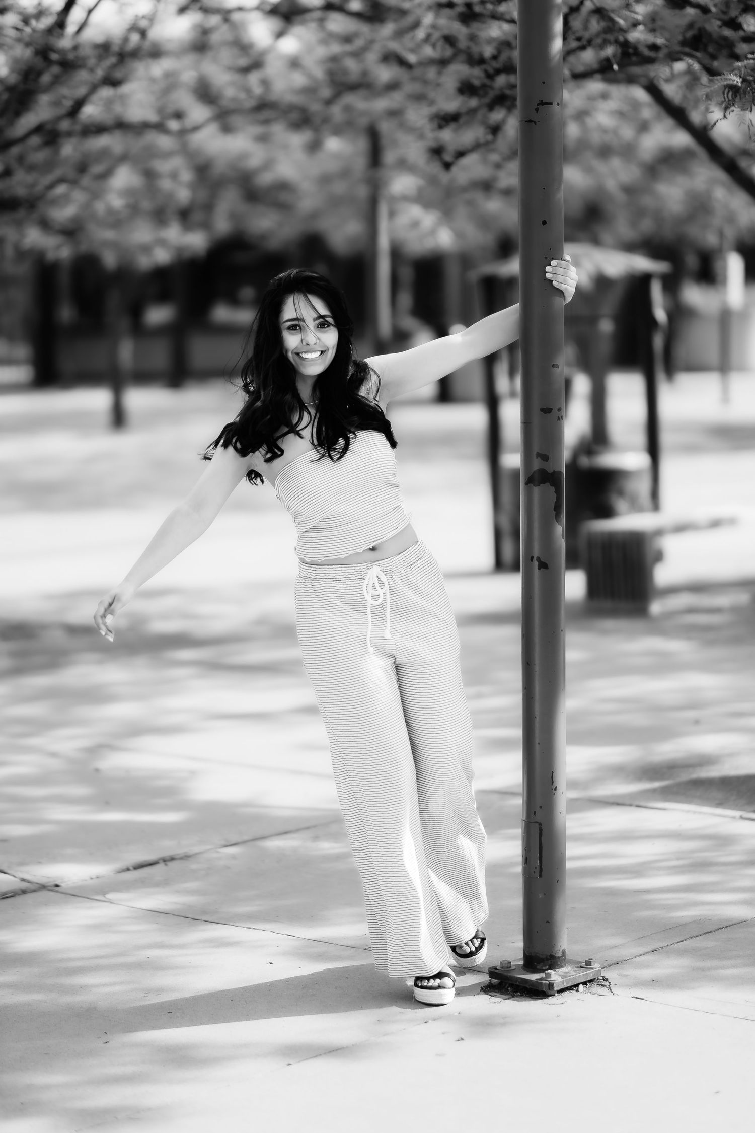 A playful black and white portrait holding onto a street pole in casual attire.