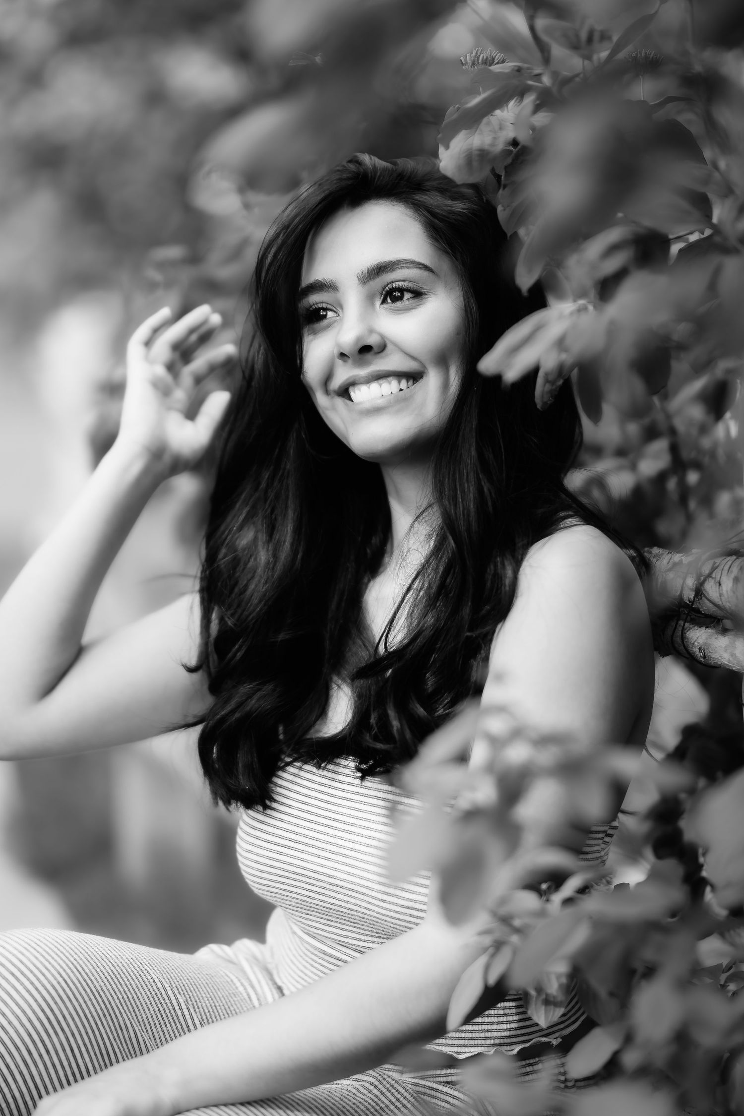 A joyful black and white portrait with natural lighting framed by soft leaves and branches.
