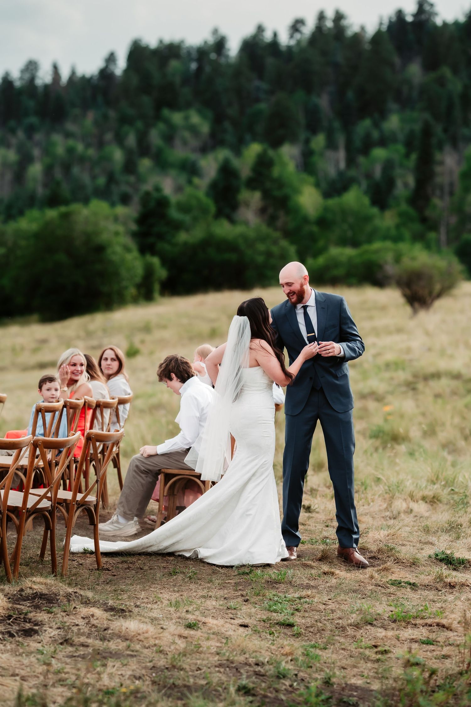 Rustic outdoor wedding ceremony with wooden chairs on hillside overlooking mountains.