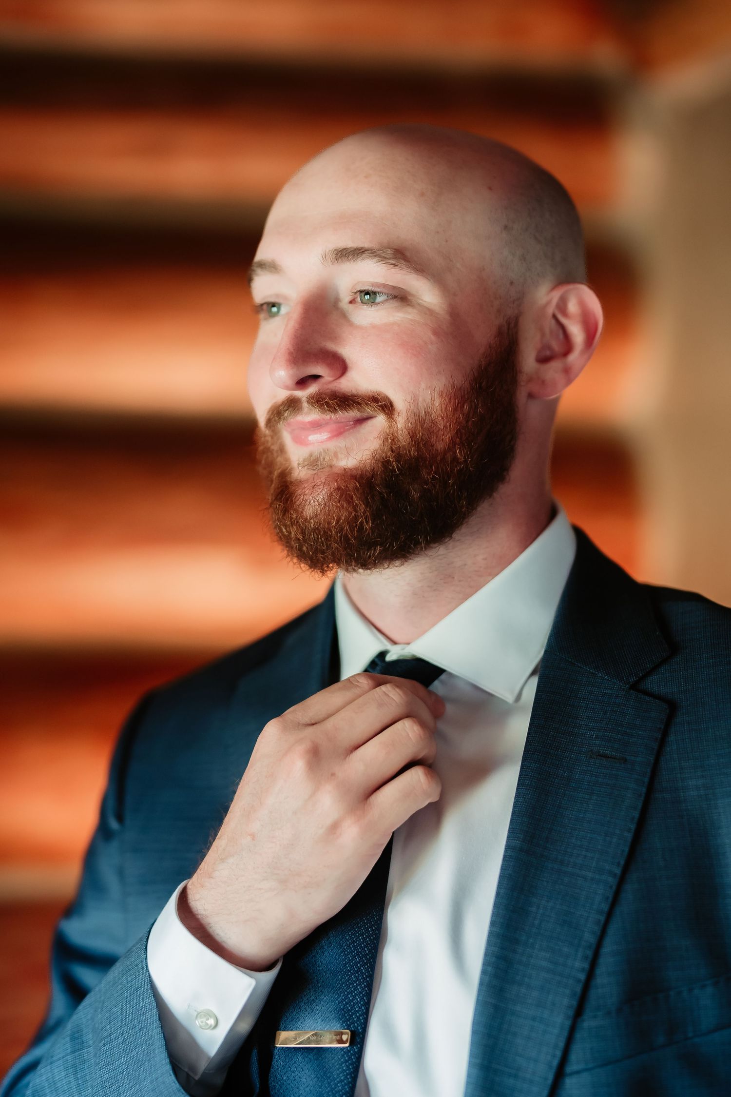 A close-up series of shots showing someone in a navy suit adjusting their red beard in warm lighting.