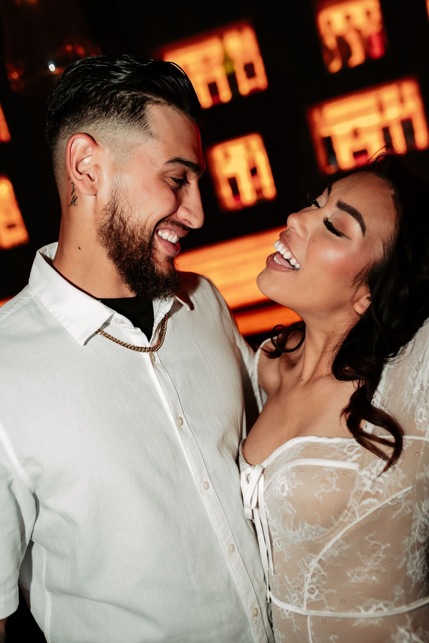 A romantic couple shares joyful laughter against glowing orange lights in the background.