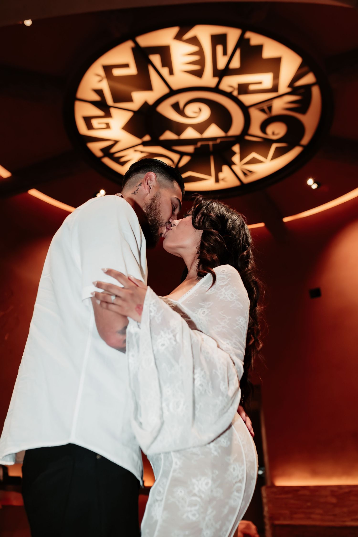 A couple shares their first dance under a decorative illuminated ceiling medallion.