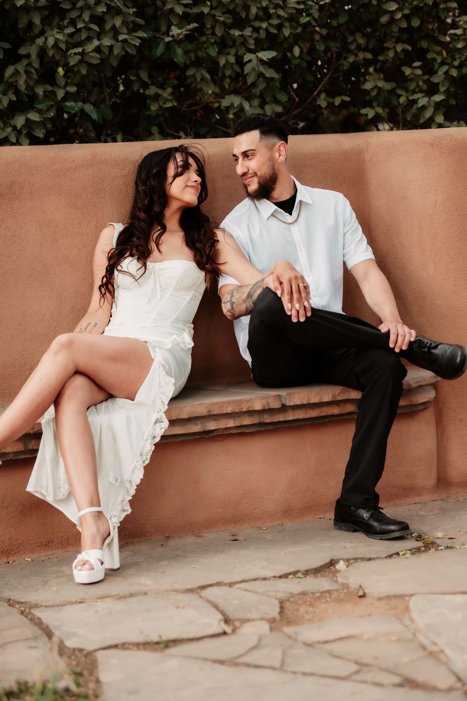 Casual couple's portrait session showing relaxed poses on a stone bench with greenery backdrop.