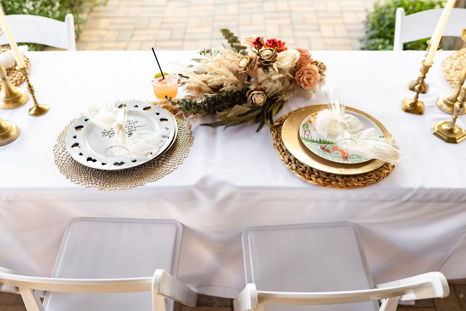 Elegant wedding table setting with gold chargers, white linens, and dried floral centerpiece.