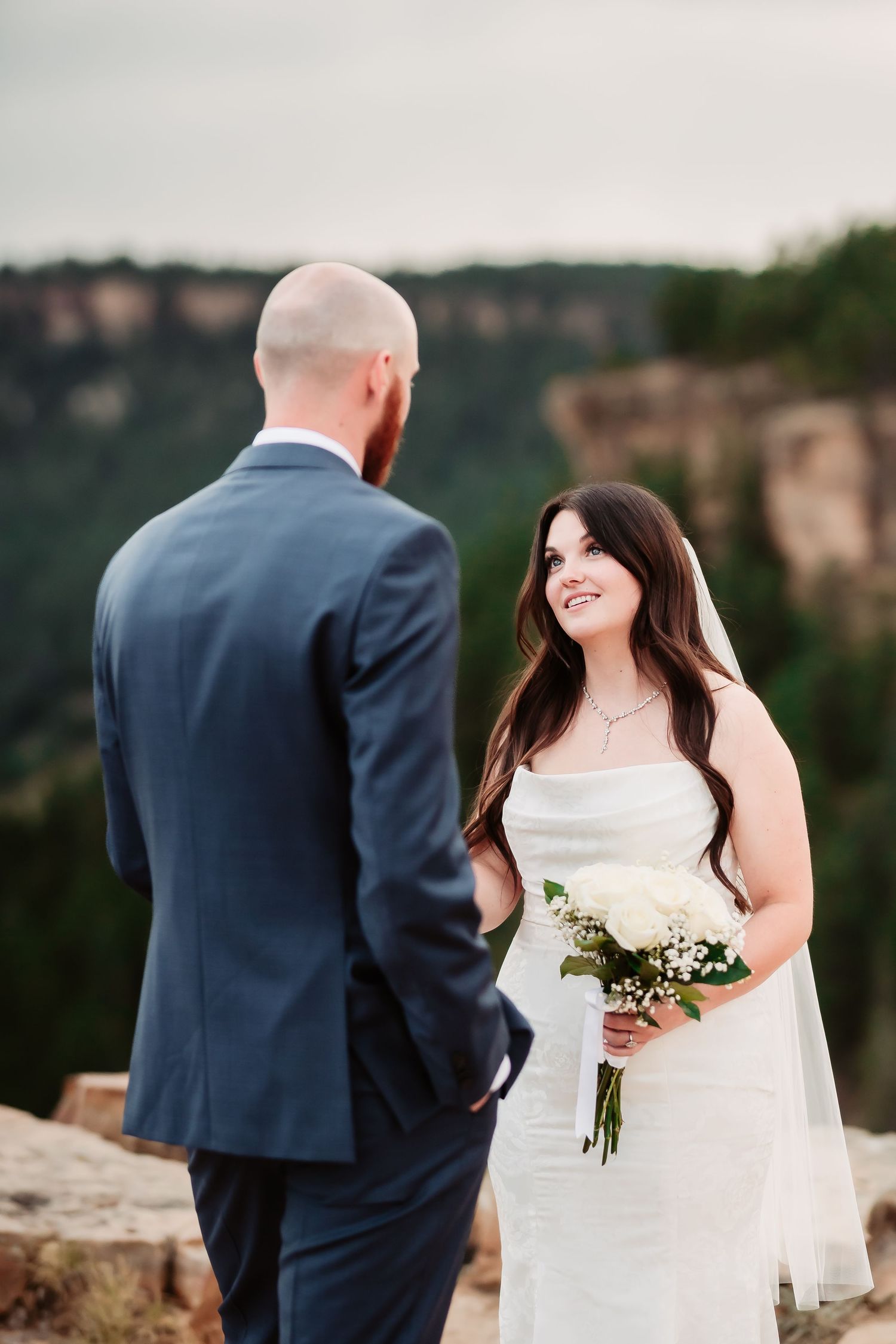 A romantic wedding exchange on a scenic mountain overlook with dramatic cliffs in the background.