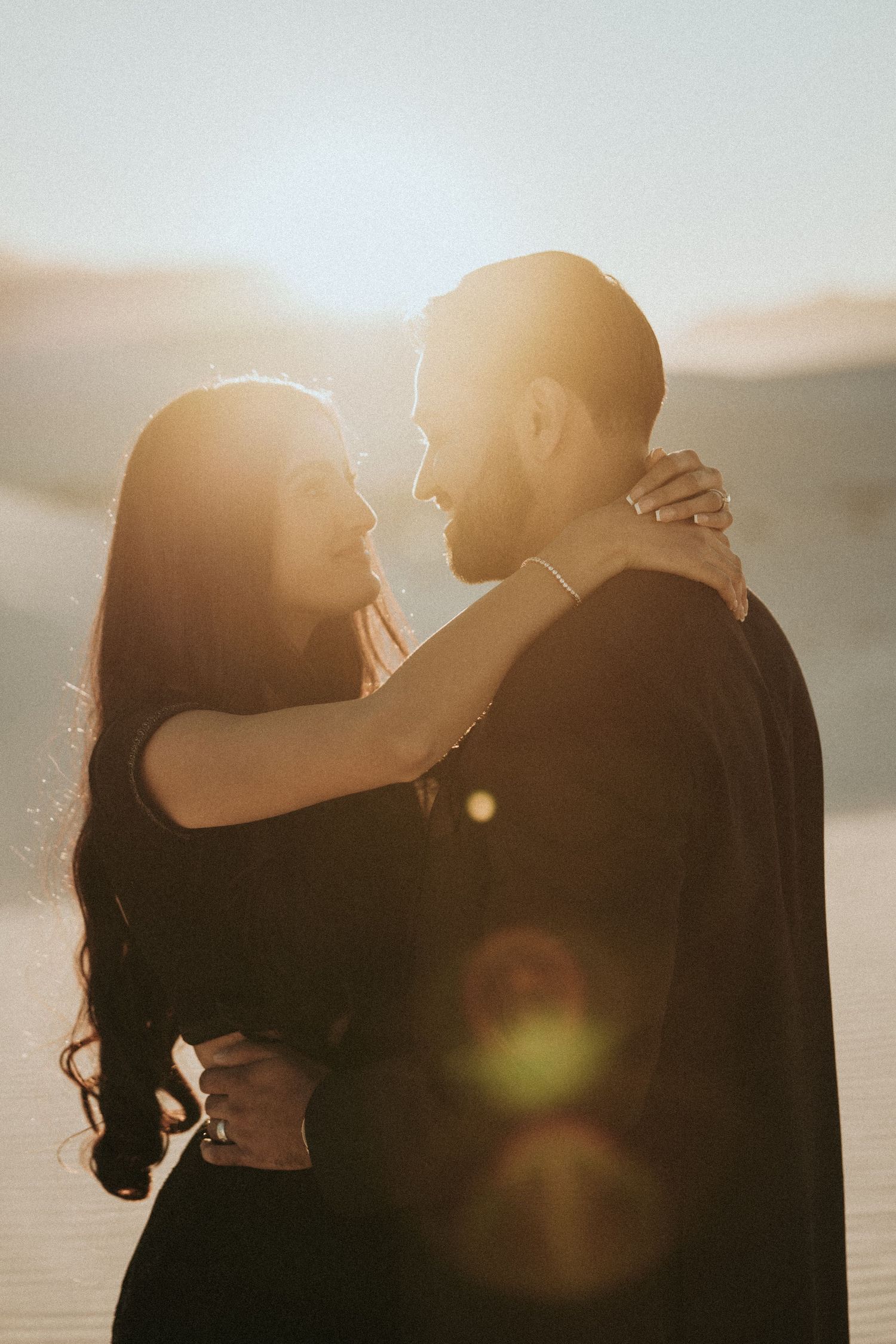 Romantic silhouette of a couple embracing in warm sunset light with lens flare effect.