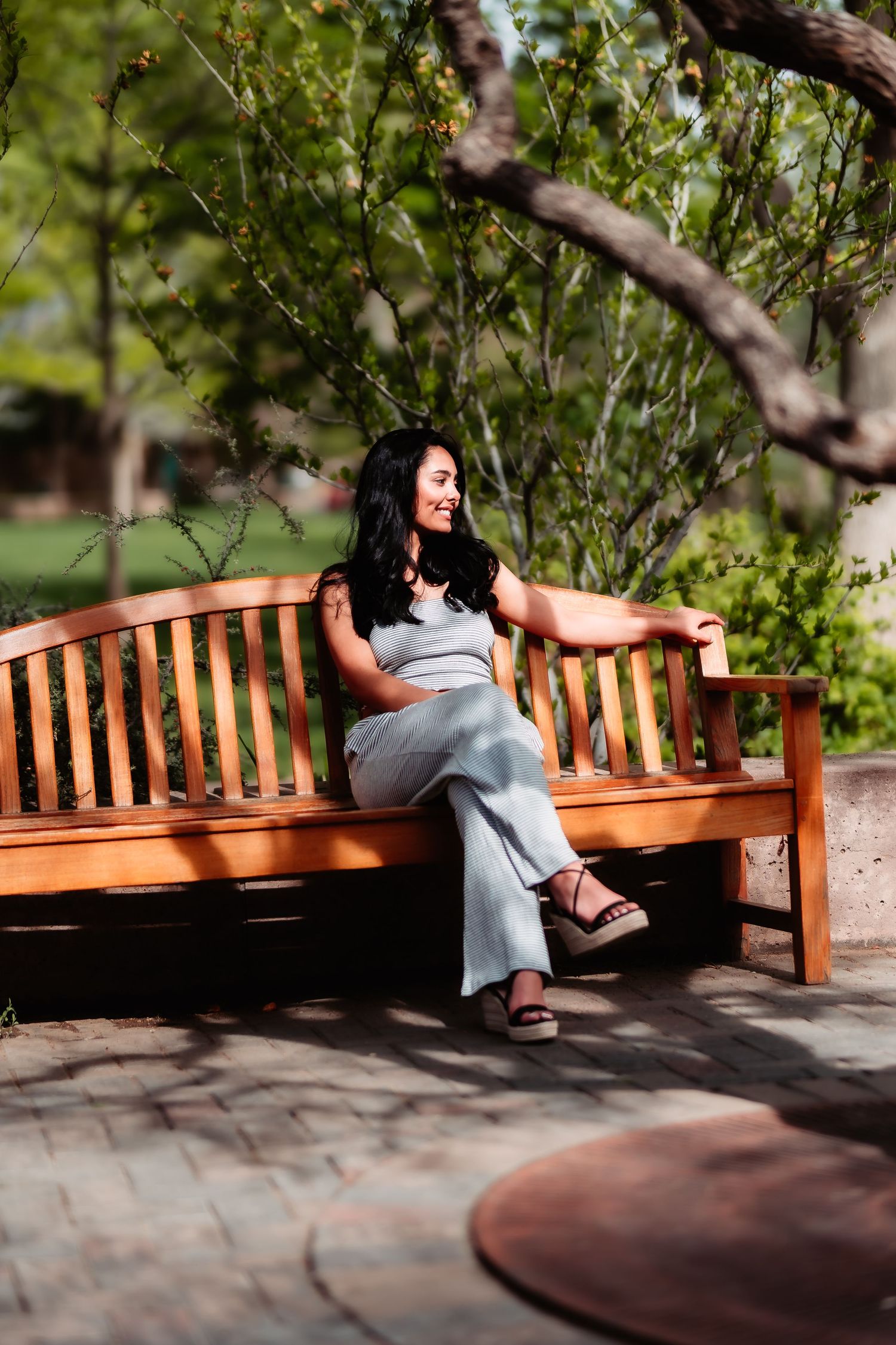 A woman in casual attire relaxes on a wooden bench in a garden setting.